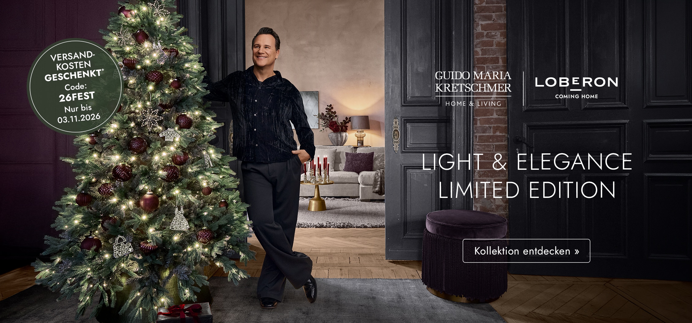 Mann lehnt an beleuchtetem Weihnachtsbaum mit bordeauxfarbenen Kugeln in elegantem Wohnzimmer mit Weihnachtsdeko