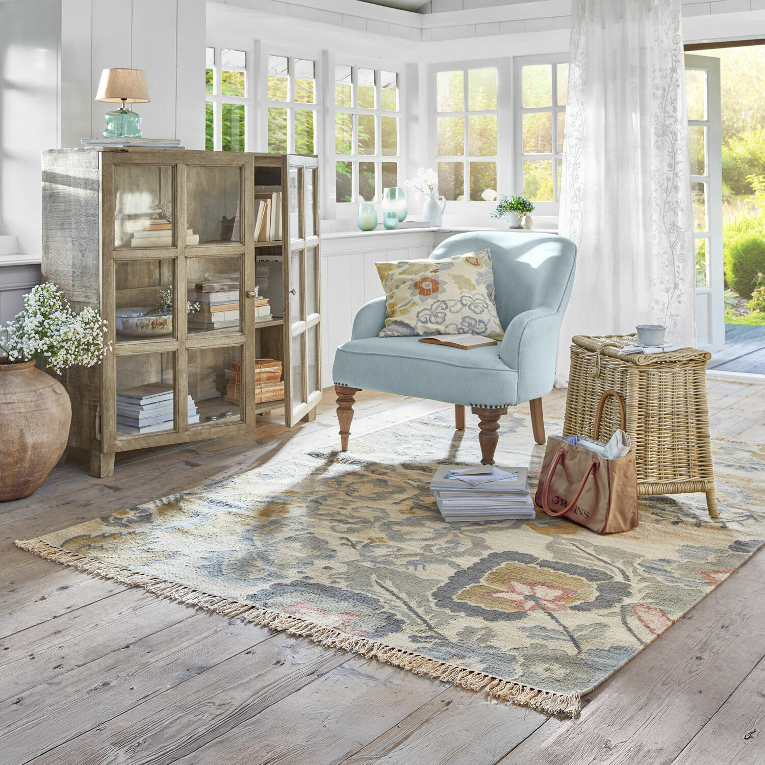 Teppich Sussex Helles Wohnzimmer mit hellblauem Sessel, Holzvitrine und floralem Teppich auf hellem Parkettboden