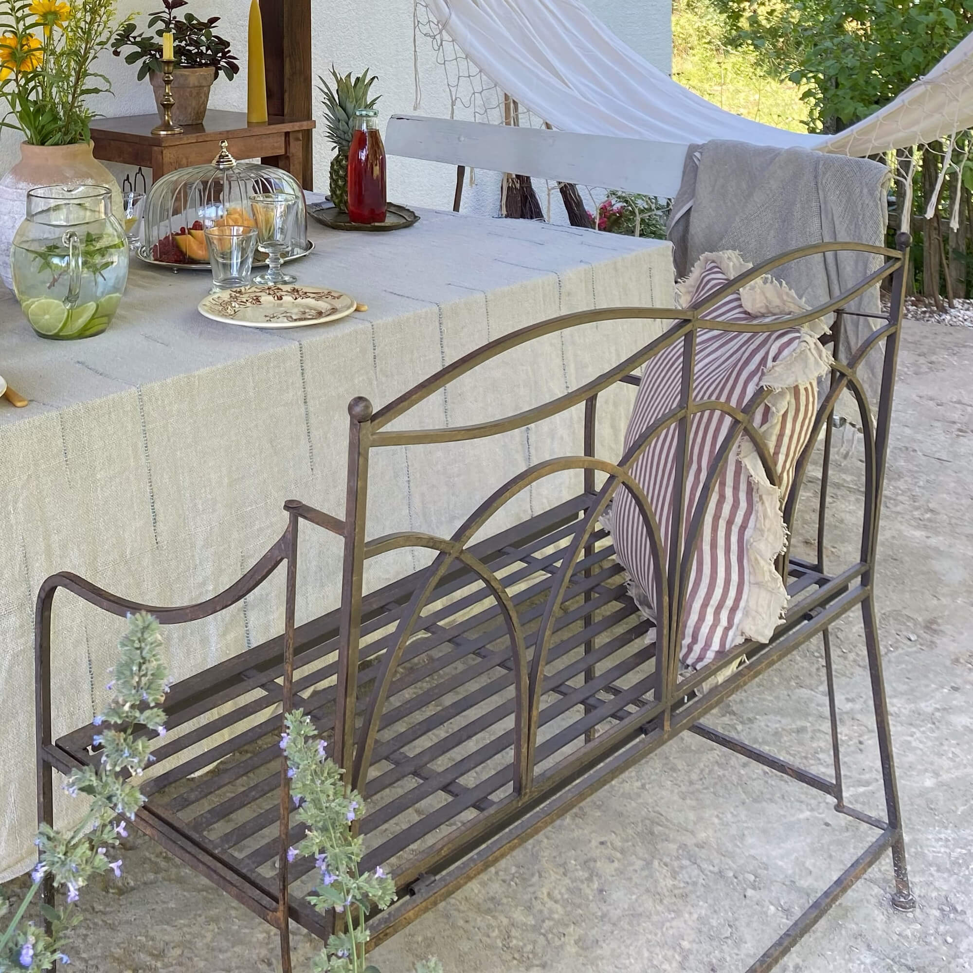 Metall-Gartenbank im Vintage-Stil mit gestreiftem Kissen und natürlicher Aussendekoration