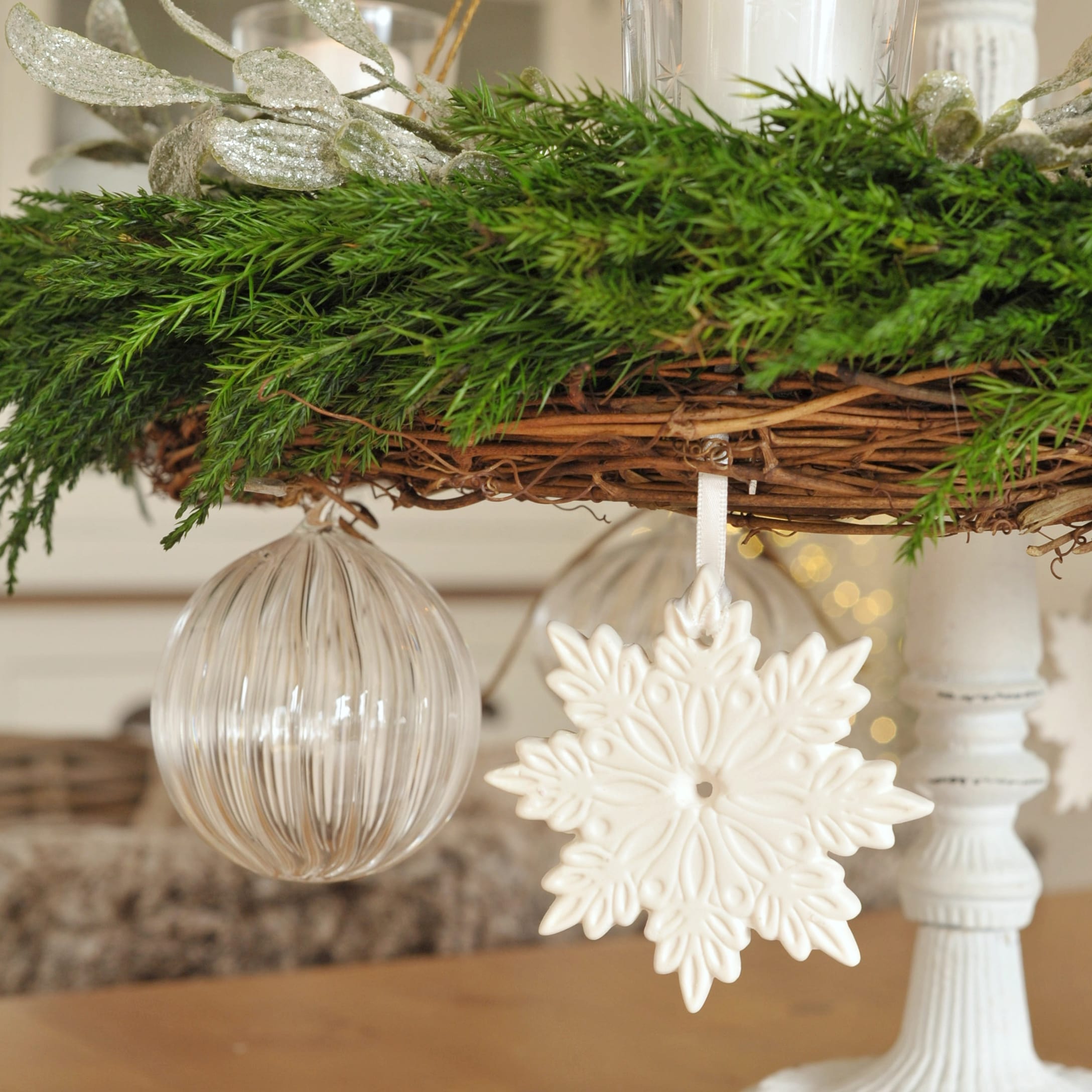 Weisser Keramik-Schneeflockenanhänger und transparente Glaskugel an grünem Adventskranz aus Weide