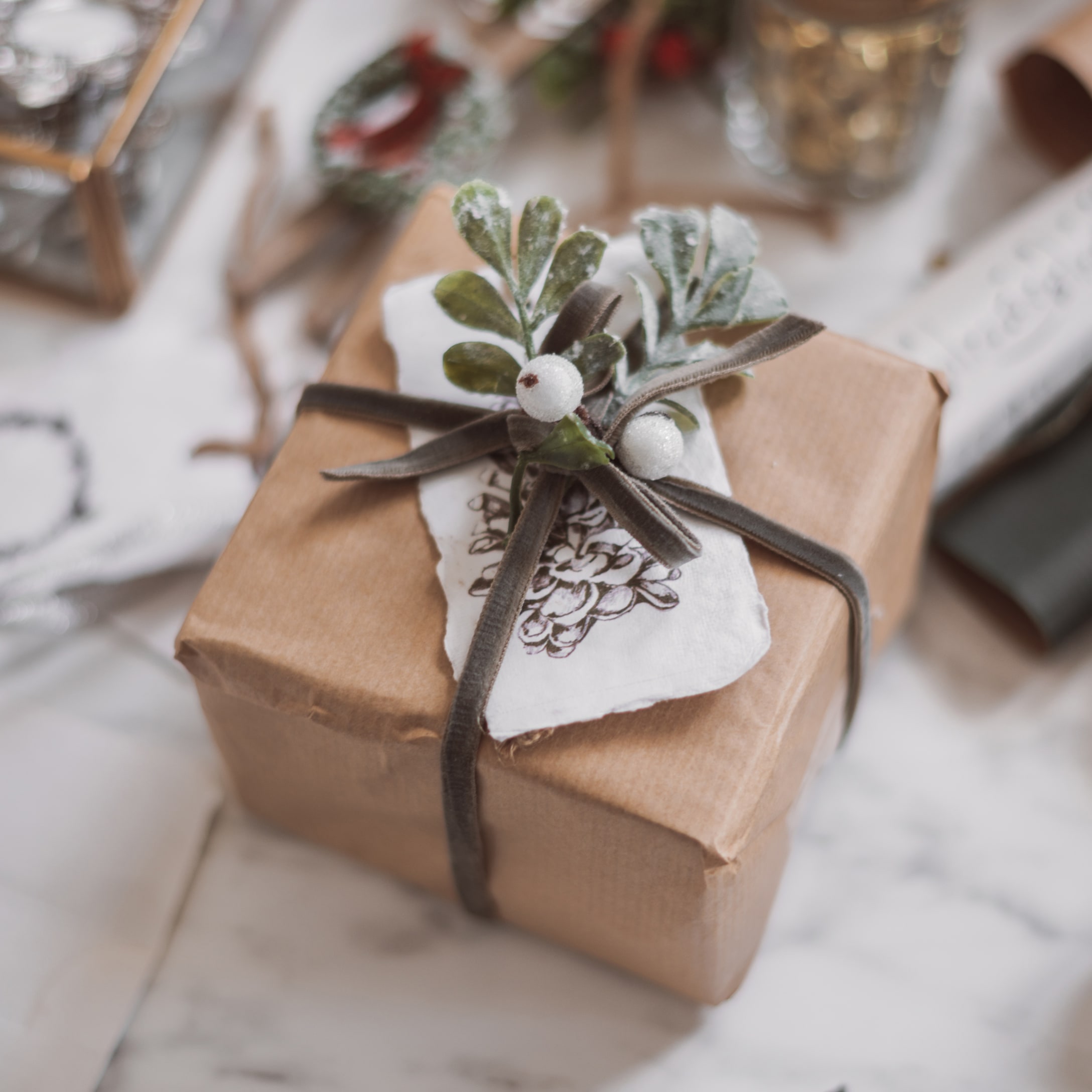Geschenk in braunem Packpapier mit dekorativem Zweig und weissen Beeren auf Samtschleife
