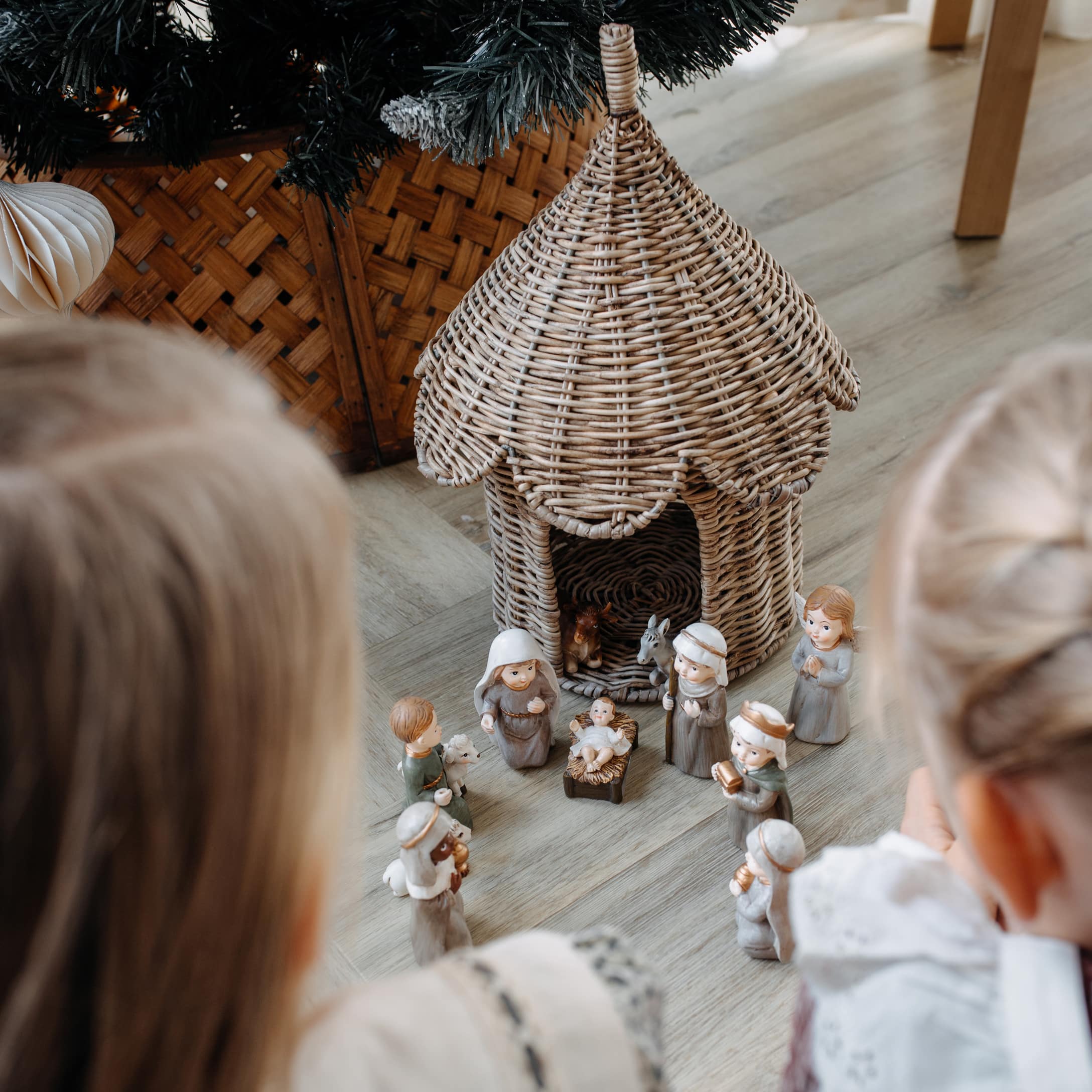 Kinder betrachten Weihnachtskrippe mit Keramikfiguren und einem Korbhaus auf dem Boden