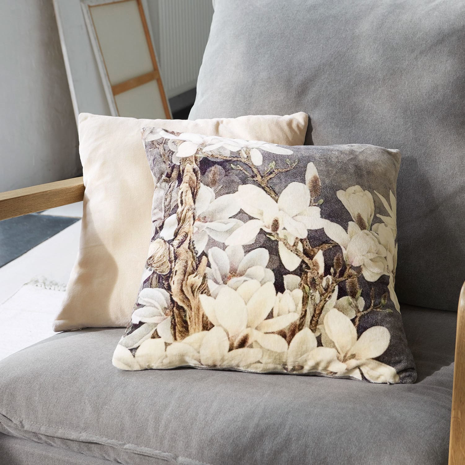 Dekoratives Kissen aus weichem Material mit floralem Muster in Beige- und Grautönen auf dem Sofa