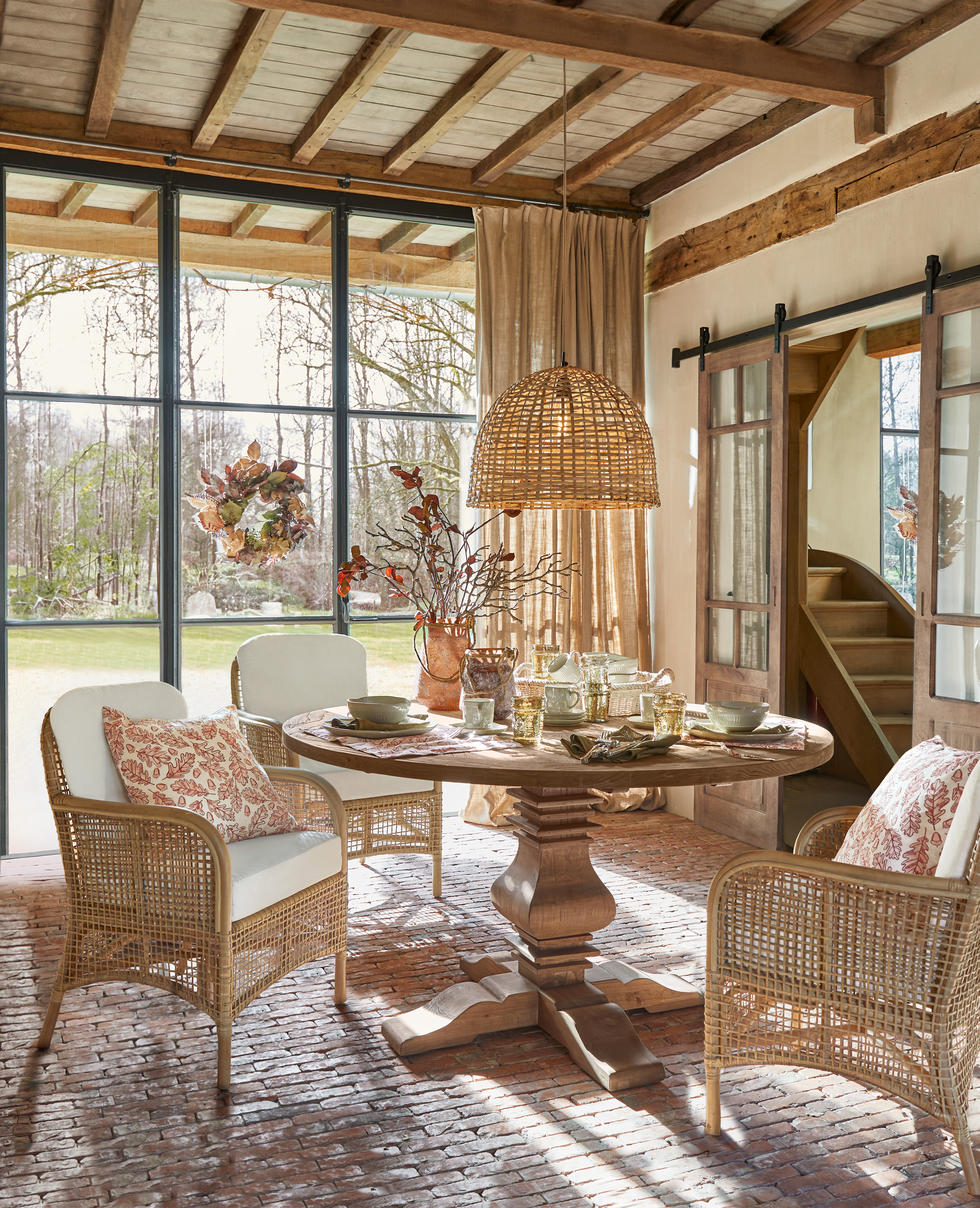 Esszimmer mit rundem Holztisch und Rattanstühlen mit weissen Kissen und Dekorationen