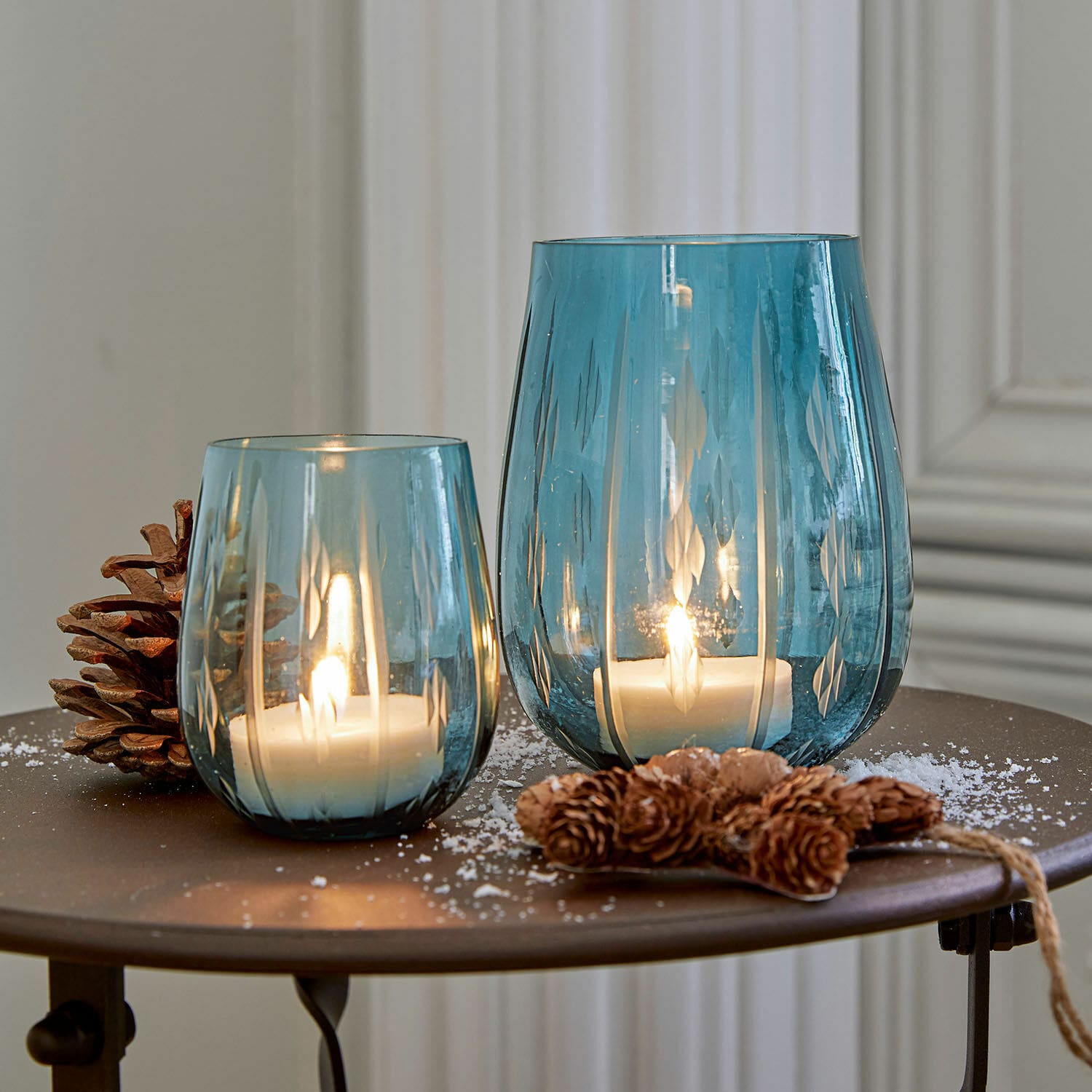 Windlicht 2er Set Danisar Zwei blaue Glaswindlichter mit Muster, weissen Kerzen und Kiefernzapfen-Dekoration auf dem Tisch