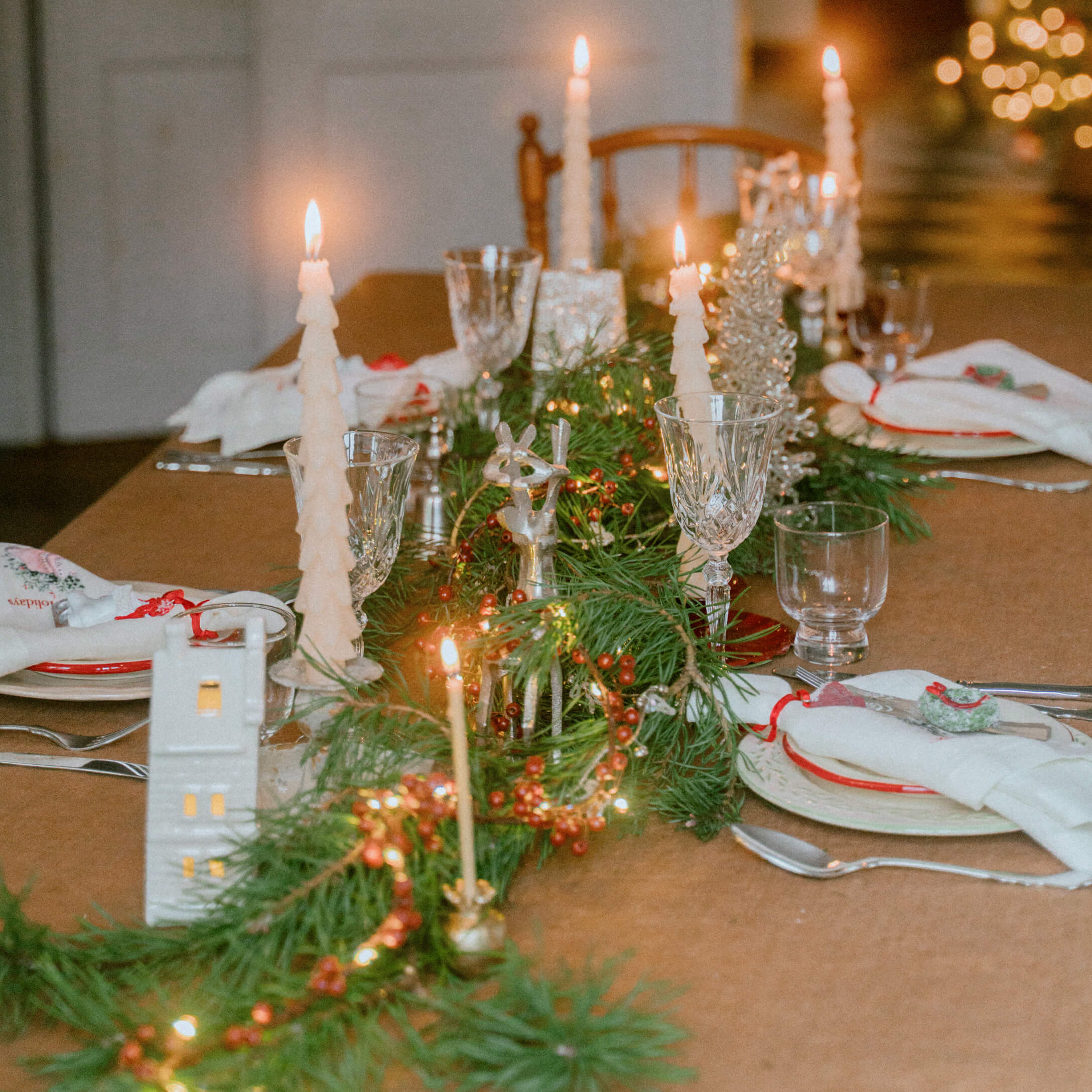 Festlich gedeckter Tisch mit grünen Zweigen, roten Beeren und weissen Tannenbaumkerzen für Weihnachtsdekoration