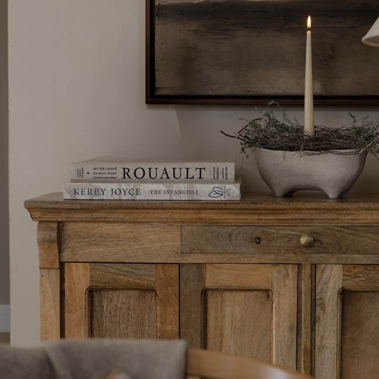 Holzkommode mit zwei Büchern und brennender Kerze in Keramikschale auf dekorativem Tisch