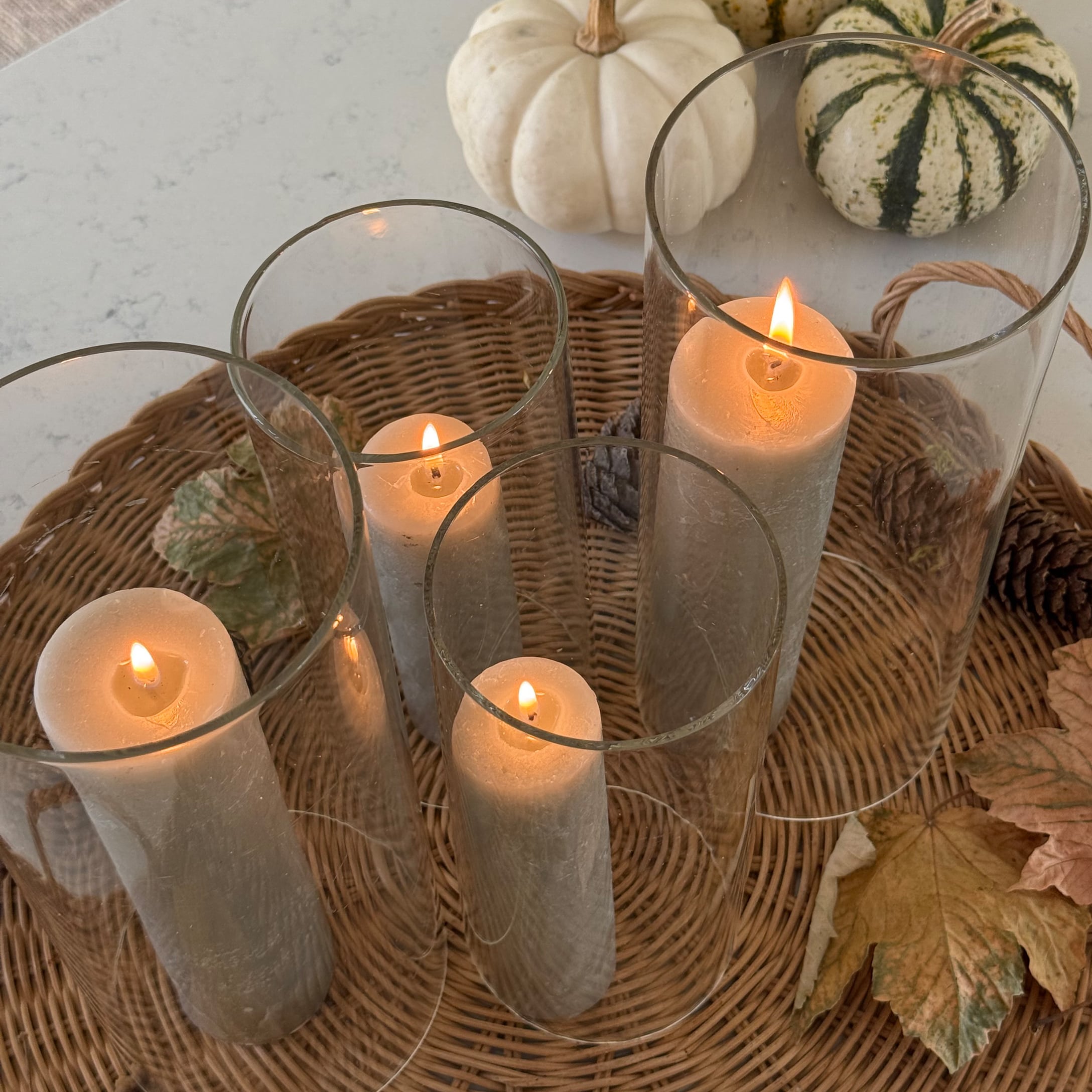 Vier weisse Kerzen in Glaszylindern auf einem Korbtablett mit Herbstblättern und Kürbissen