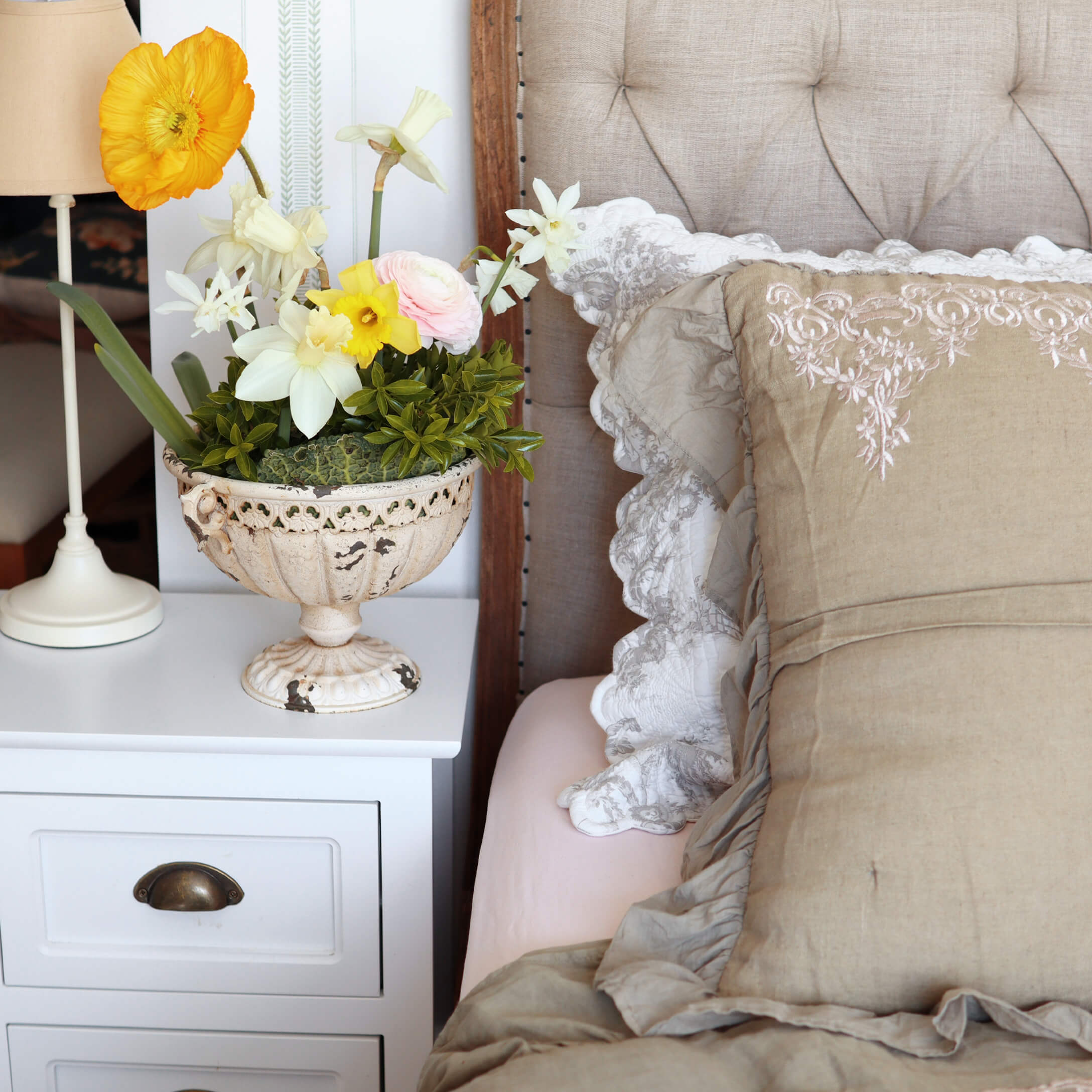 Dekorative weisse Keramikvase mit bunten Blumen auf weissem Nachttisch neben dem Bett