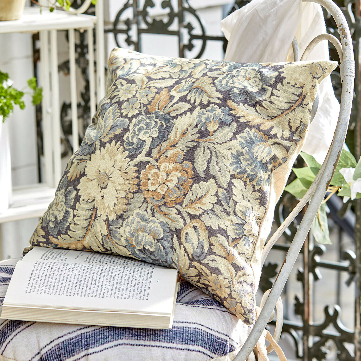 Kissenhülle Lumielle Dekoratives Kissen aus Stoff mit Blumenmuster in Beige- und Blautönen auf weissem Metallstuhl