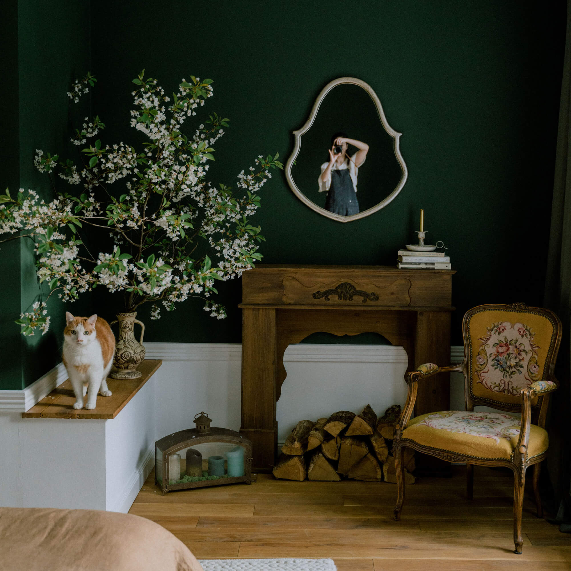 Gemütliches Wohnzimmer mit dunkelgrüner Wand, Holzkamin, gelbem Blumenstuhl und Katze auf dem Ablagebrett