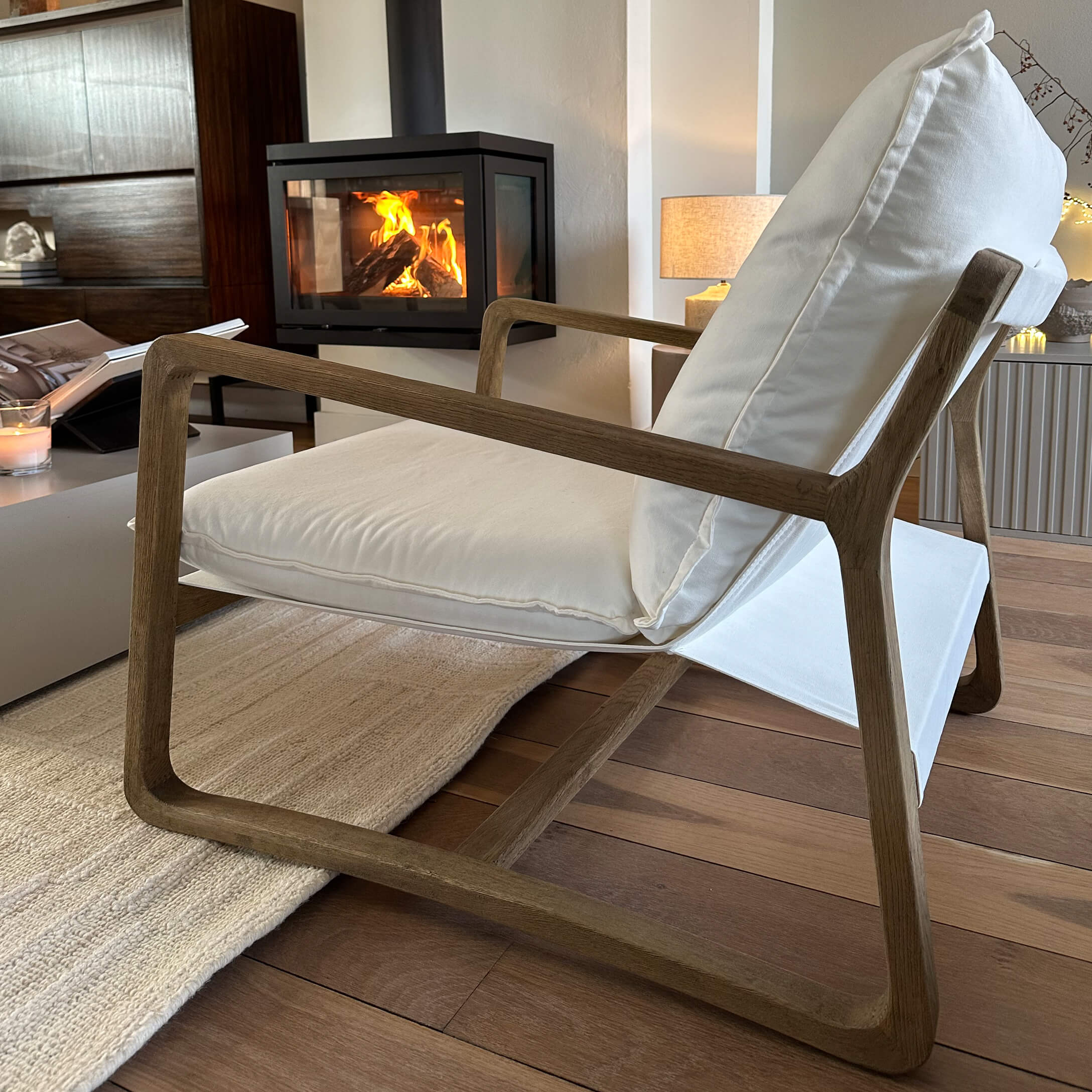 Moderner Sessel mit Holzrahmen und weissem Stoffbezug in gemütlichem Wohnzimmer mit Cheminée