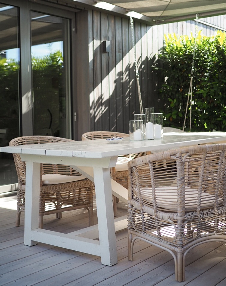 Weisser Holztisch mit natürlichen Rattanstühlen und Kerzen auf der Terrasse im Freien