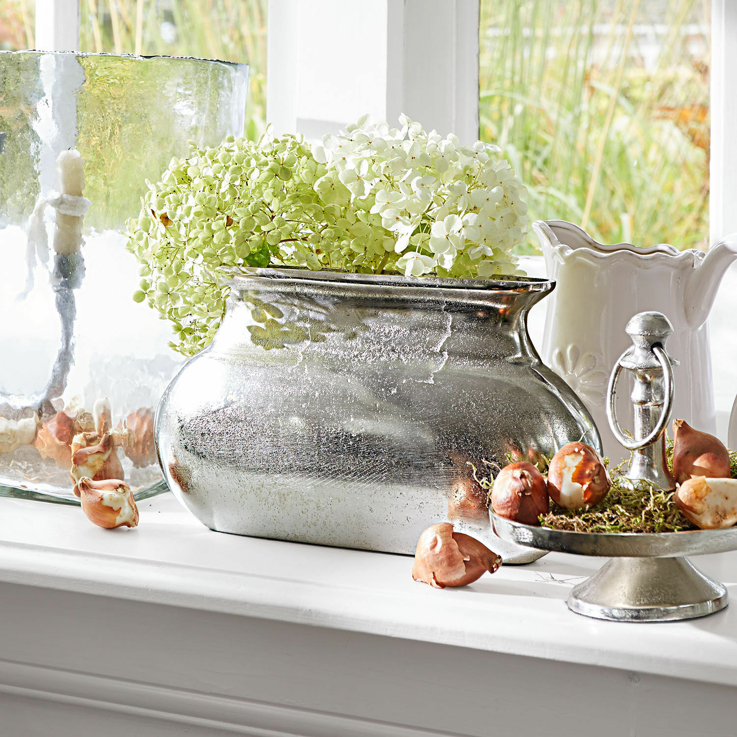 Vase Melisique Silberne Metallvase mit grün-weissen Hortensien auf der Fensterbank mit dekorativen Zwiebeln