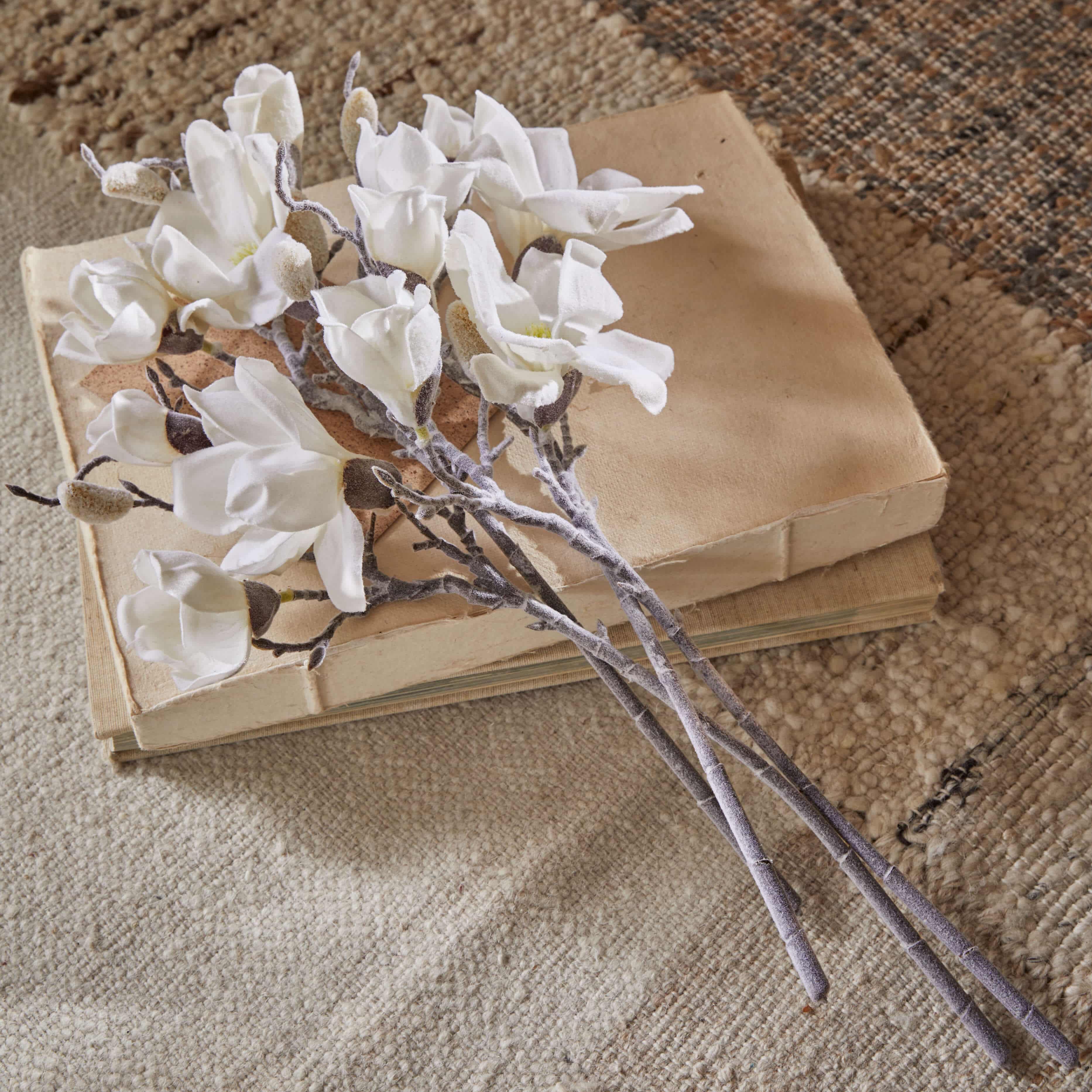 Strauß weiße Magnolienblüten aus Stoff auf alten beigen Büchern auf Teppich