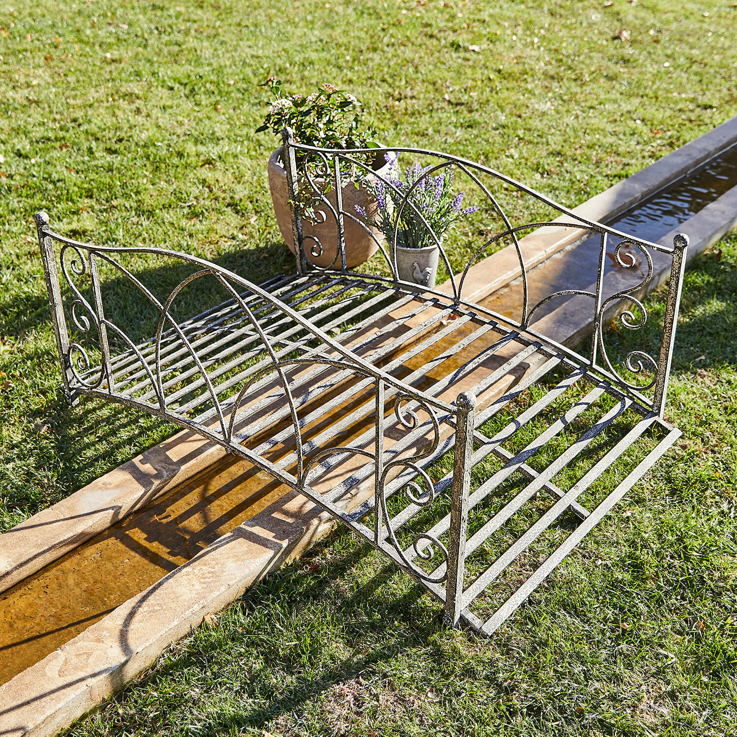 Deko-Brücke Escàs Schöner Gartenbrücke aus Metall in antik-silberner Farbe über Wasserlauf auf Rasenfläche