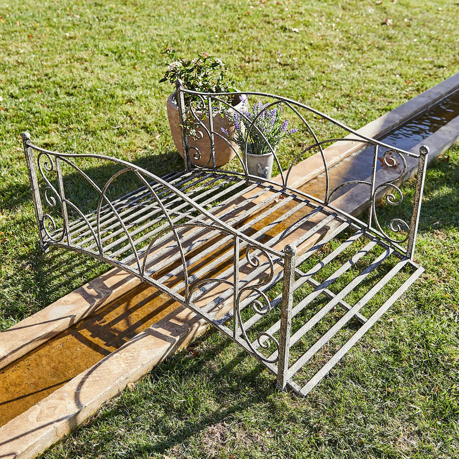 Deko-Brücke Escàs Schöner Gartenbrücke aus Metall in antik-silberner Farbe über Wasserlauf auf Rasenfläche