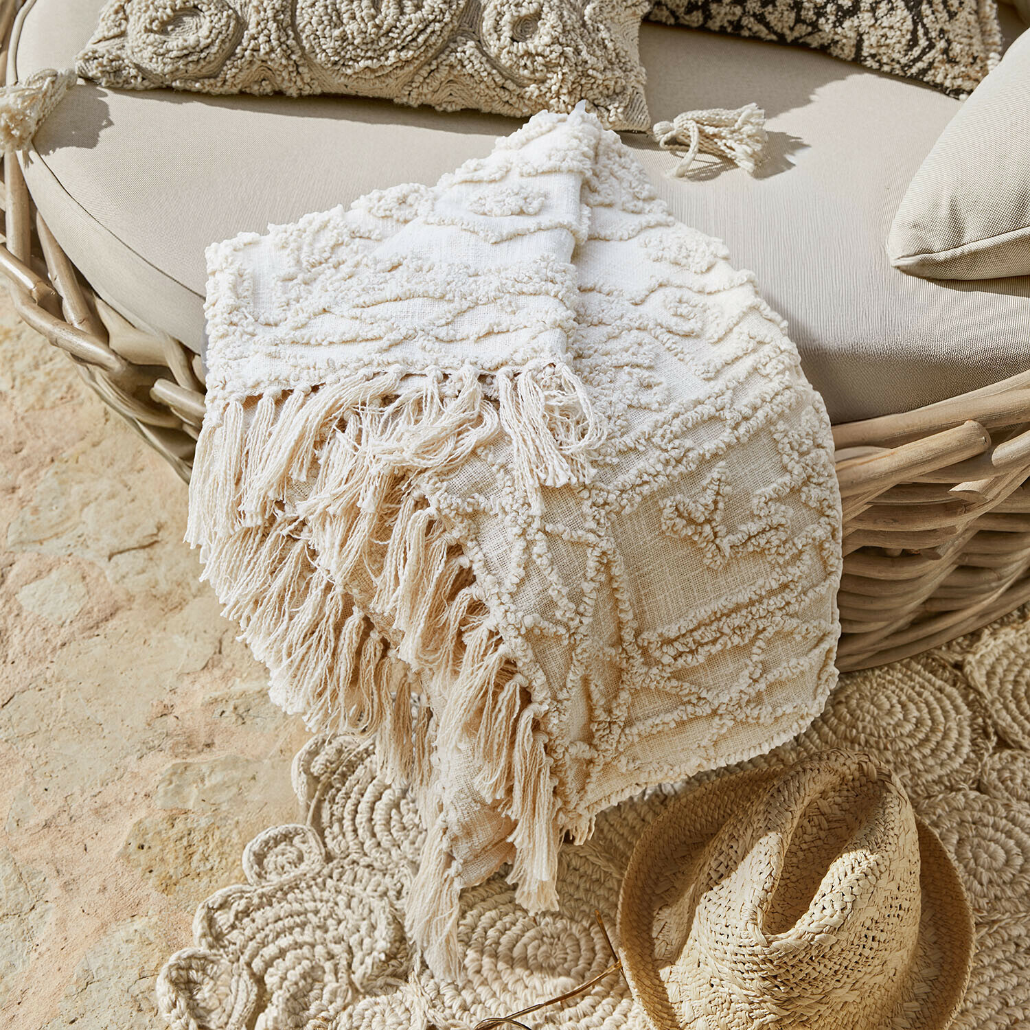 Plaid Norlinn Beige dekorative Decke mit Fransen auf Rattansessel und Strohhut auf dem Boden