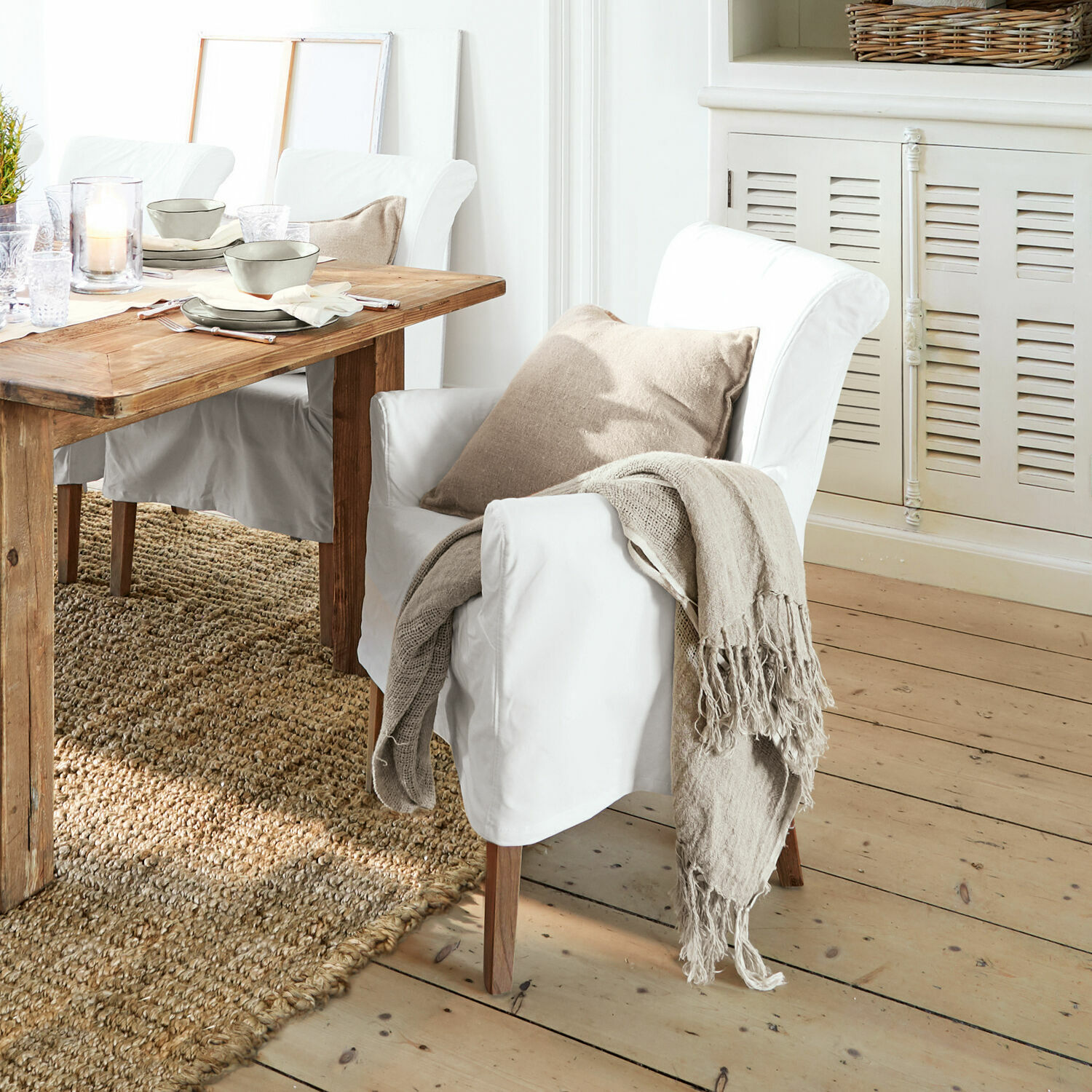 Stuhl Amherst Weisser Sessel mit Holzbeinen, beigem Kissen und naturfarbenem Plaid im Esszimmer mit Holztisch