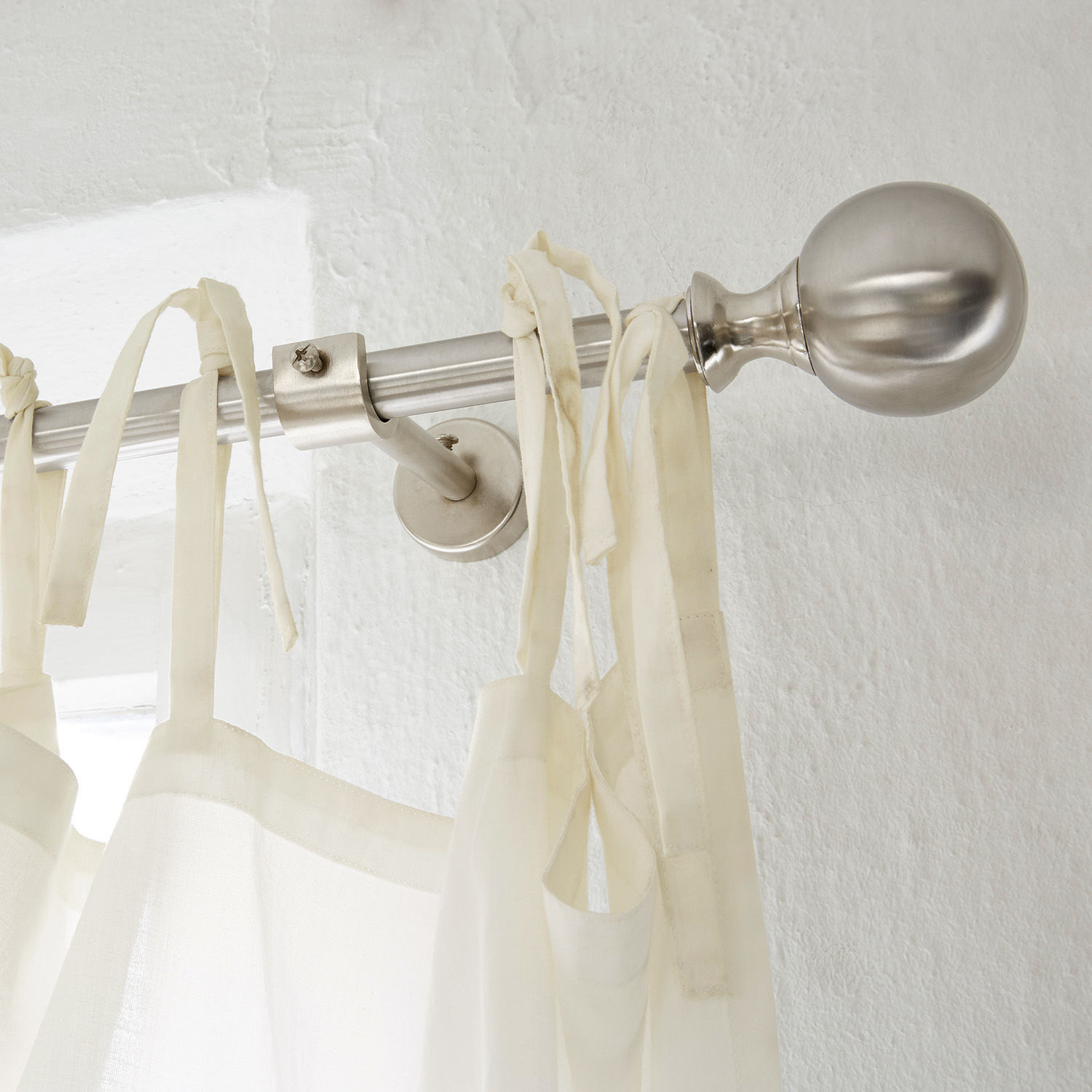 Metallene silberne Gardinenstangen mit kugelförmigem Abschluss und weissem Vorhang mit Bändern