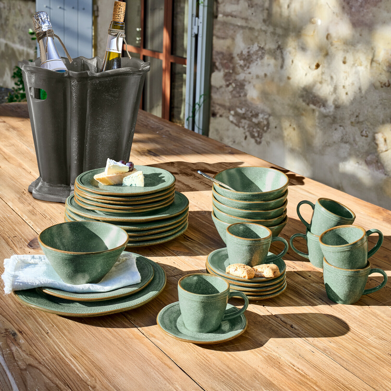 Grünes Steingut-Geschirrset auf Holztisch mit schwarzem Weinkühler daneben