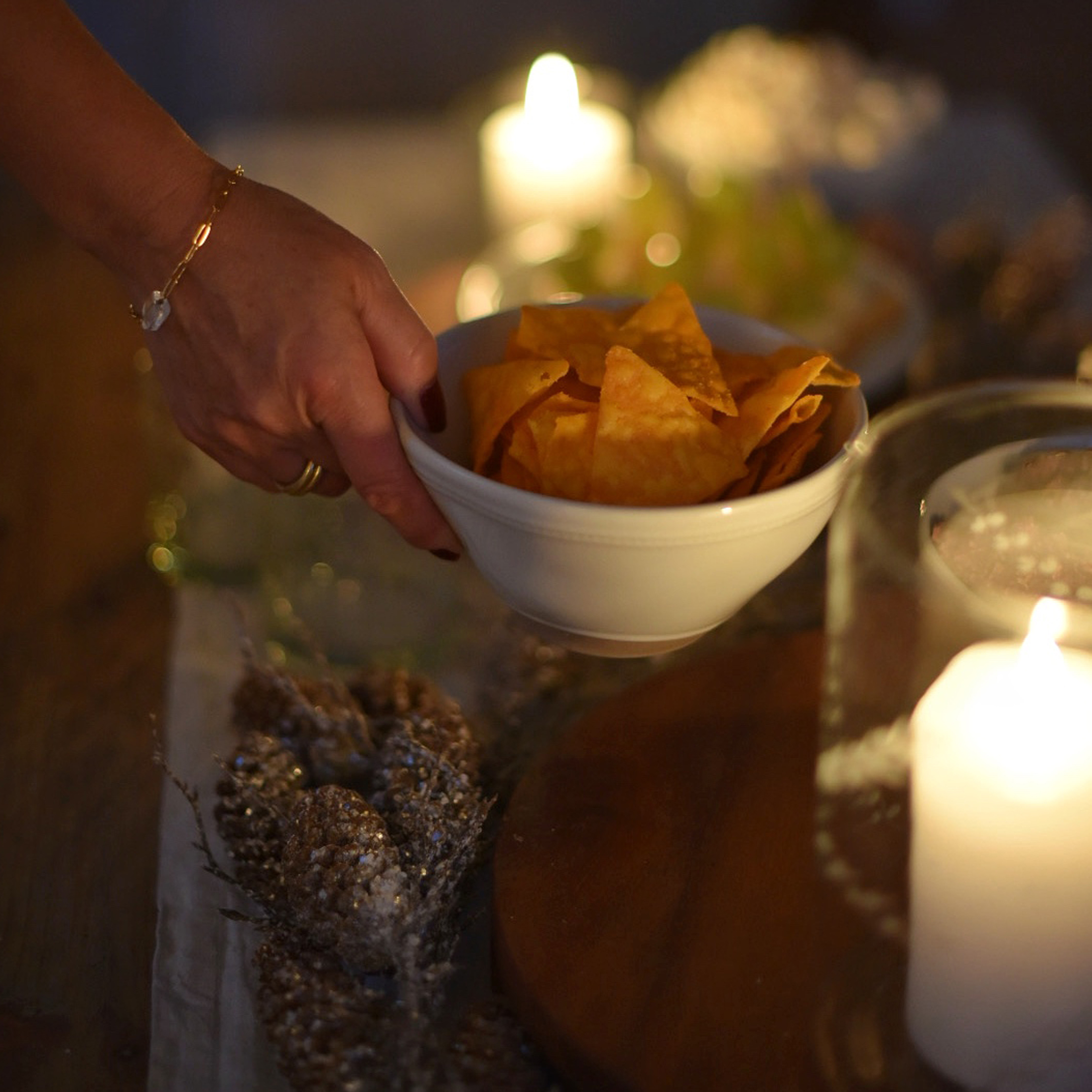 Hand hält weisse Schüssel mit orangen Chips vor Kerzenlicht und festlicher Dekoration