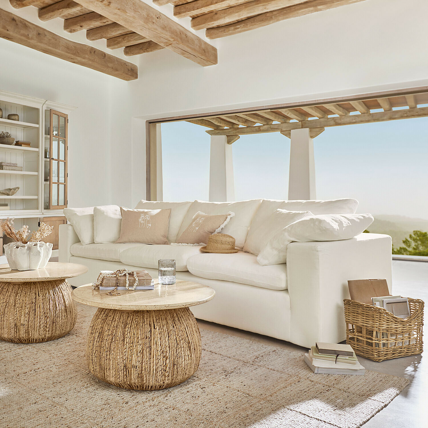 Sofa Everholt Helles Wohnzimmer mit weissem Sofa und zwei runden Couchtischen aus Holz und natürlichem Rattan