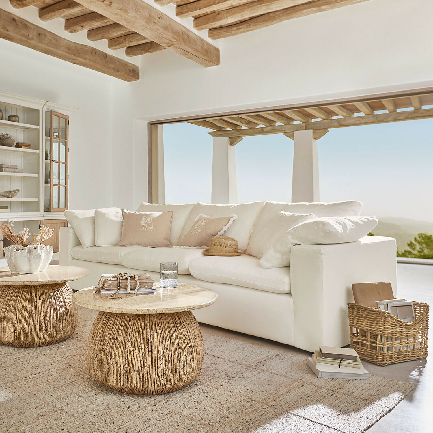 Sofa Everholt Helles Wohnzimmer mit weissem Sofa und zwei runden Couchtischen aus Holz und natürlichem Rattan