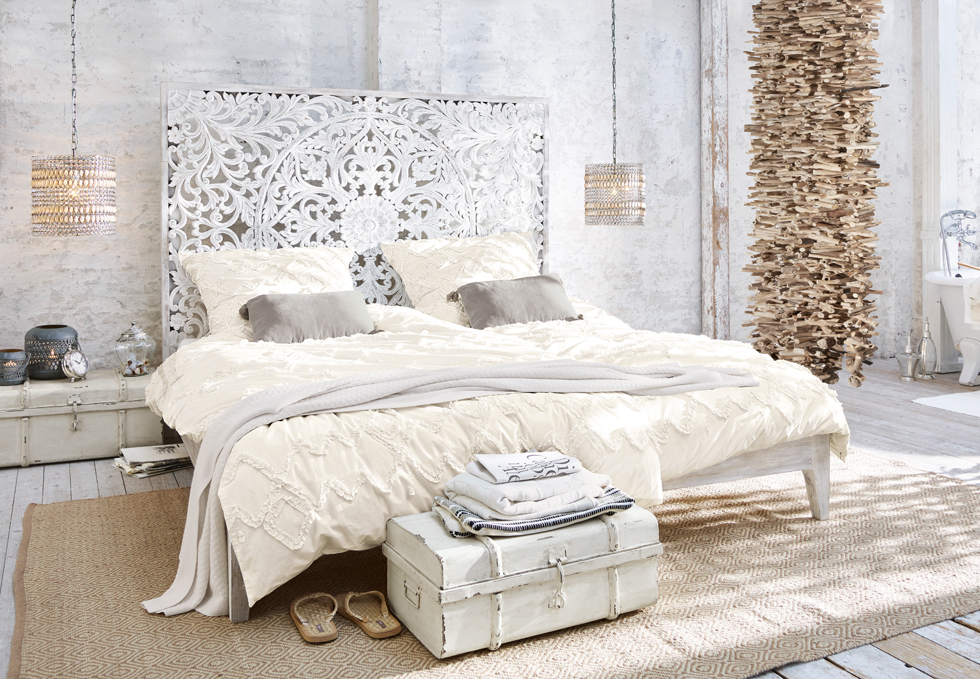 Boho-Schlafzimmer mit weissem, geschnitztem Bett, cremefarbener Bettwäsche und natürlichen Holzdekorationen