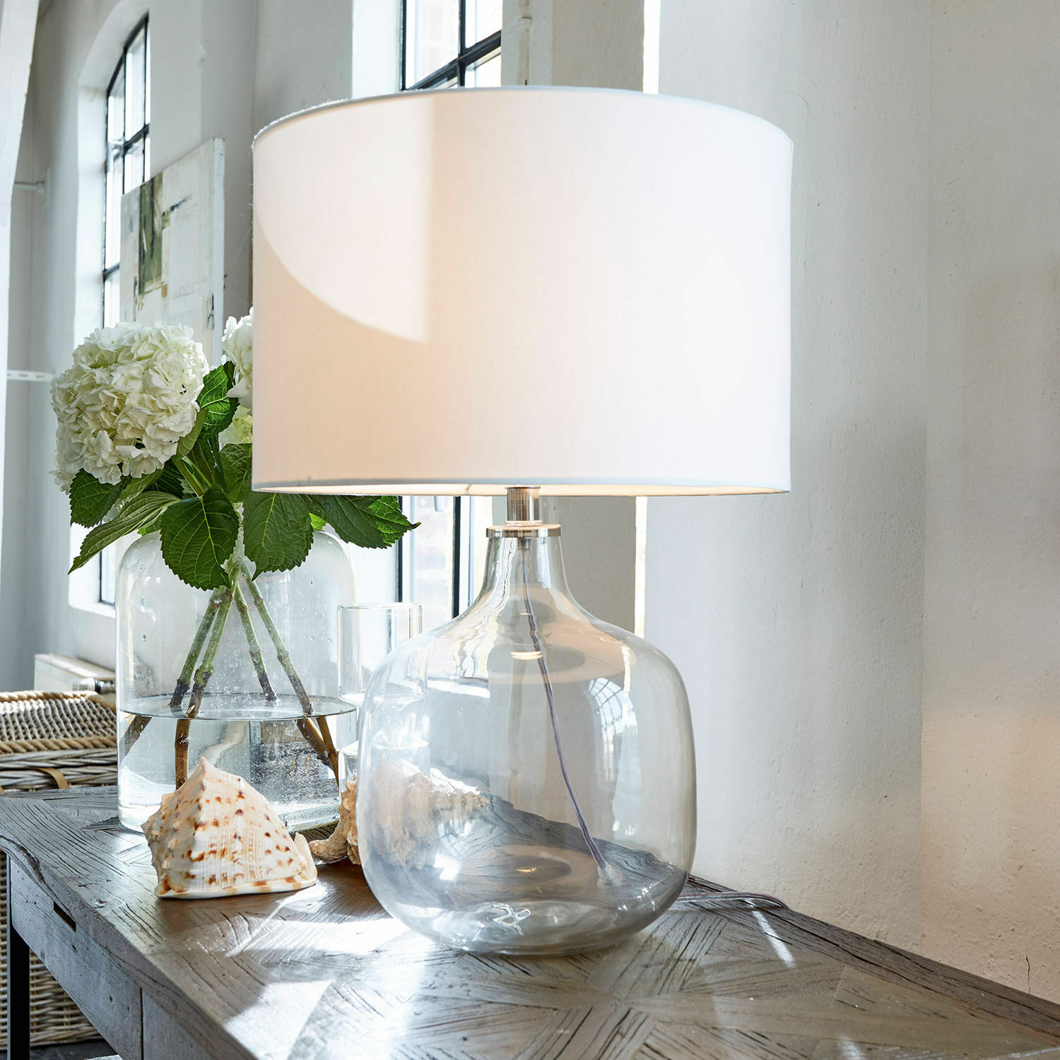 Tischlampe Malmy Tischlampe aus klarem Glas mit weissem Lampenschirm auf Holztisch mit Muscheldekor