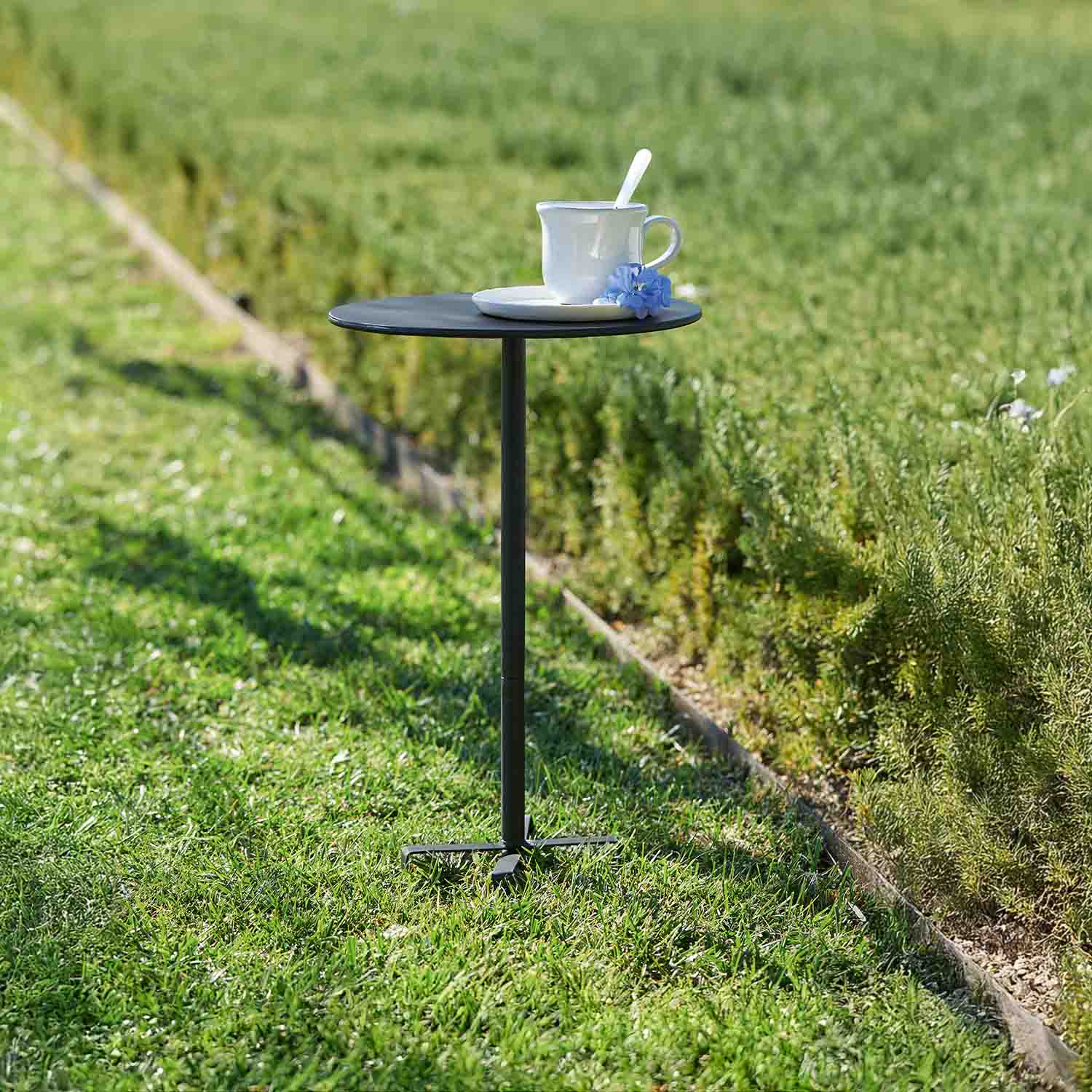 Kleiner schwarzer Metall-Gartentisch mit weisser Tasse und blauer Blume auf Gras