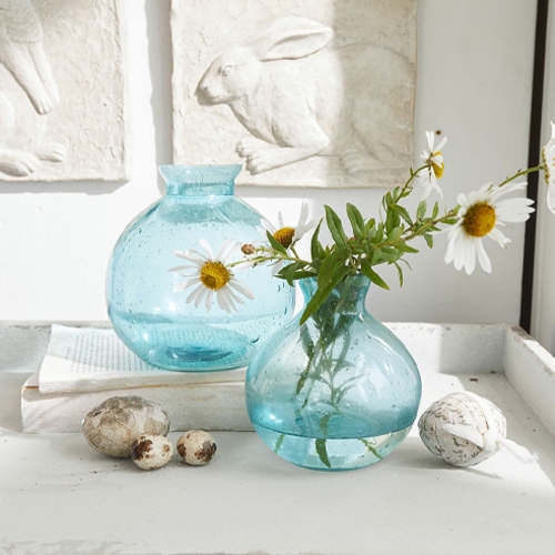 Transparente blaue Glasvasen mit Kamillenblumen als natürliche Tischdekoration