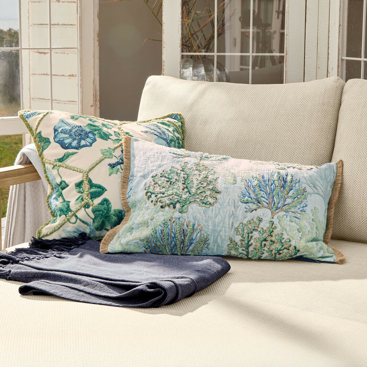 Zweifarbige Dekokissen mit Pflanzenmotiv auf cremefarbenem Sofa mit dunkelblauer Decke