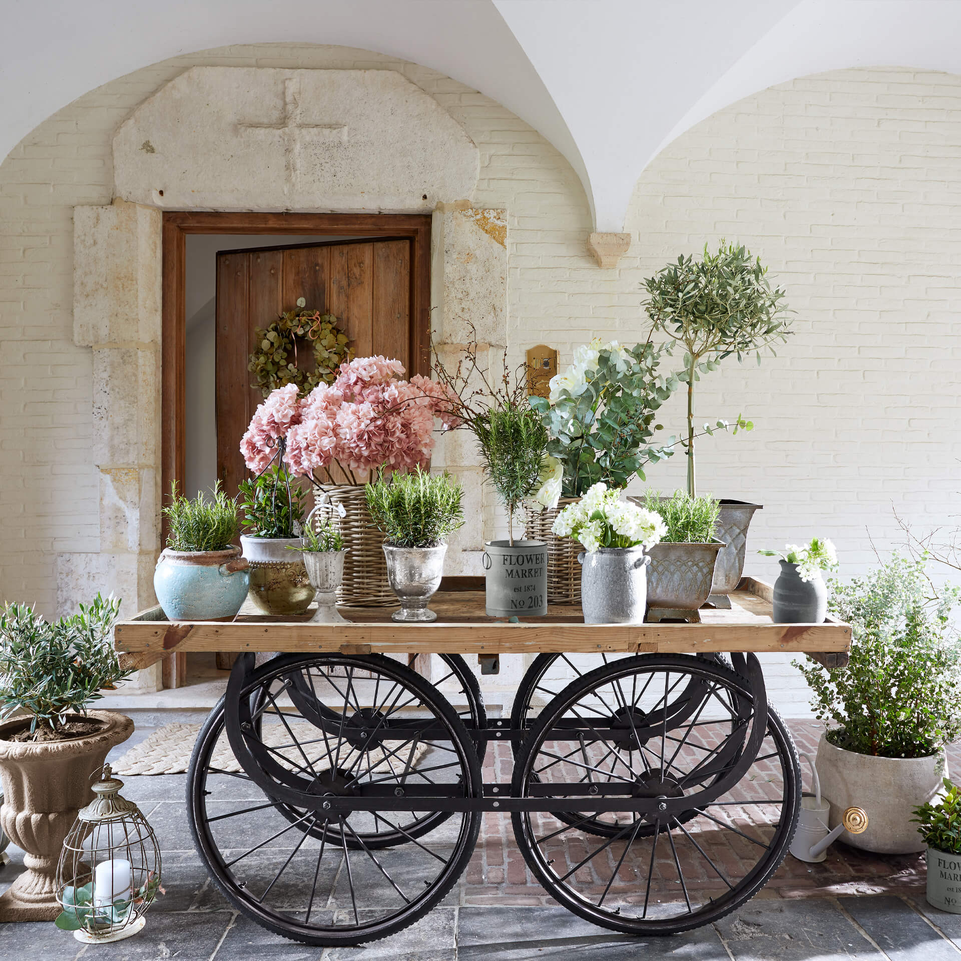 Holzwagen mit schwarzen Metallrädern, verschiedenen Metalltöpfen und rosa sowie weissen Dekoblumen