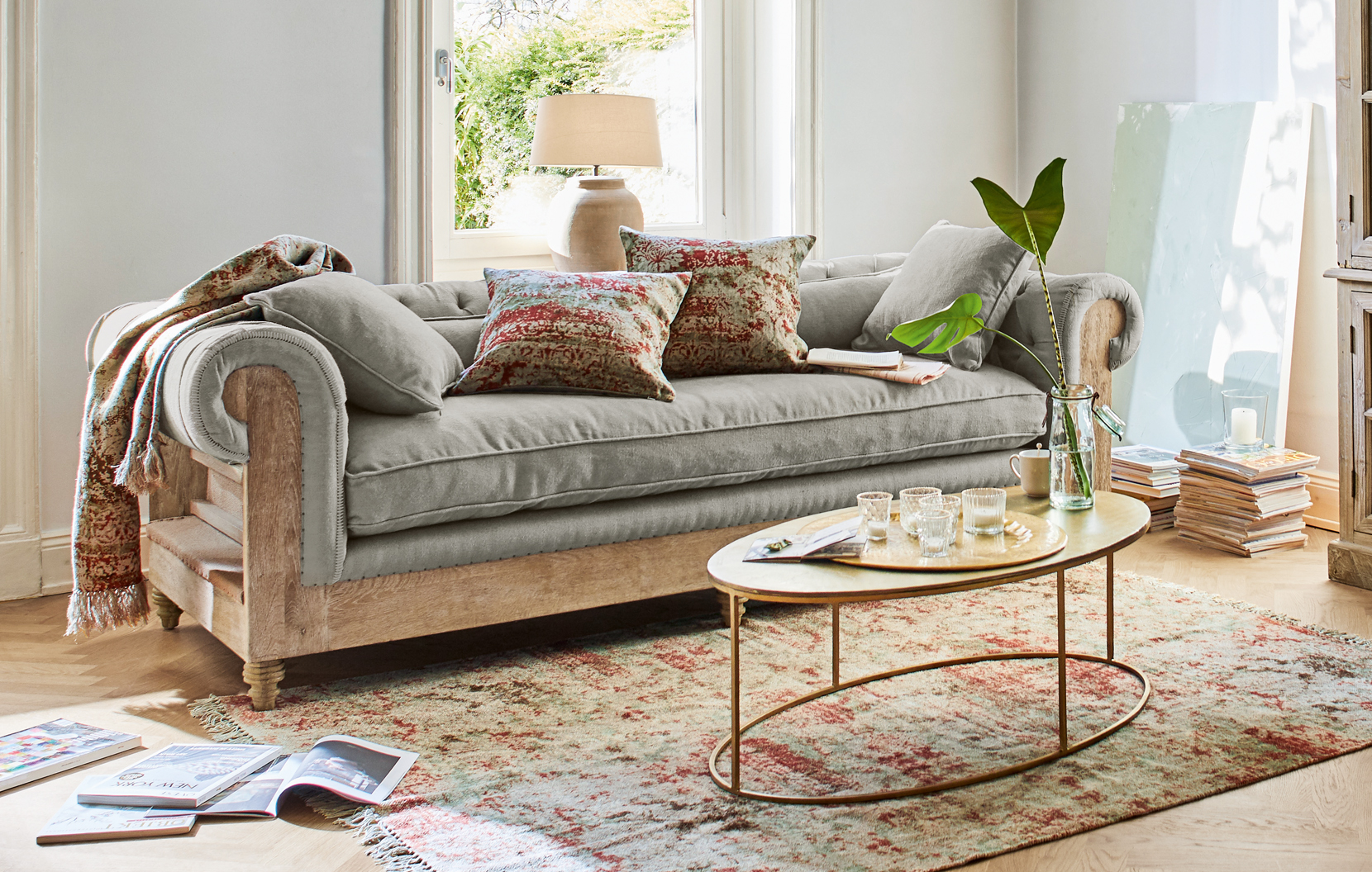 Graues Sofa mit Holzrahmen und orientalischem Teppich im hellen Wohnzimmer mit dekorativen Kissen