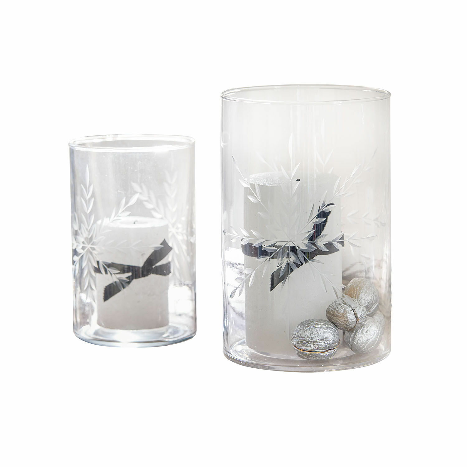 Zwei durchsichtige Glaswindlichter mit weissen Kerzen und silbernen Dekonüssen