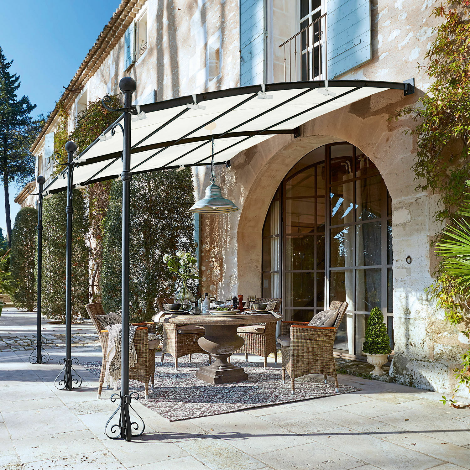 Pergola Kattles Gartenmöbel-Set aus Rattan unter weissem Vordach auf steinerner Terrasse vor einem Steinhaus