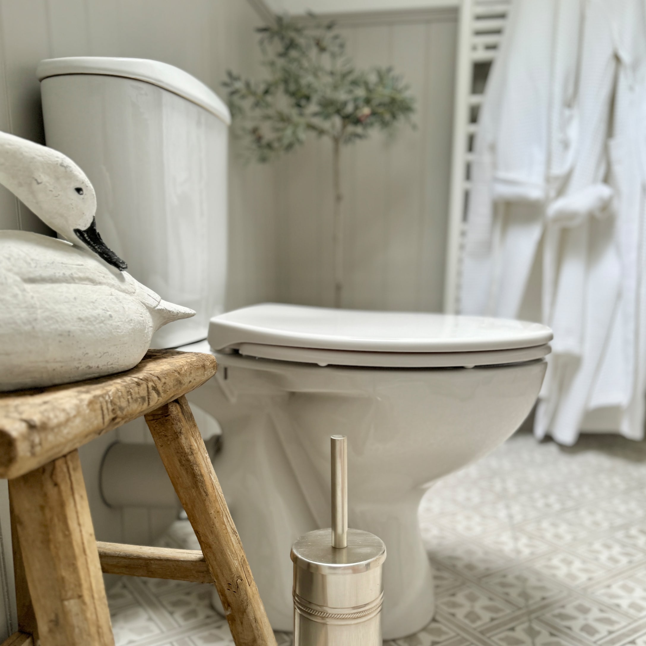 Weisse Keramiktoilette im Badezimmer mit Holzschemel und Edelstahl-Toilettenbürste