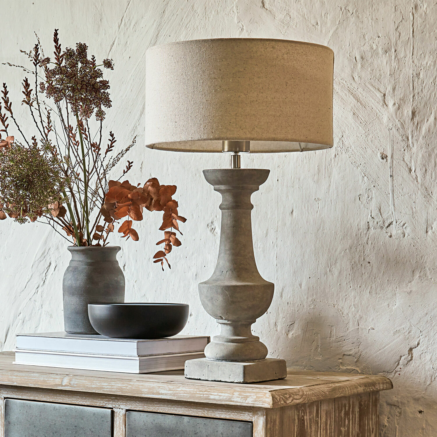 Tischlampe aus Beton mit beigem Lampenschirm auf Holzkommode mit Dekoration