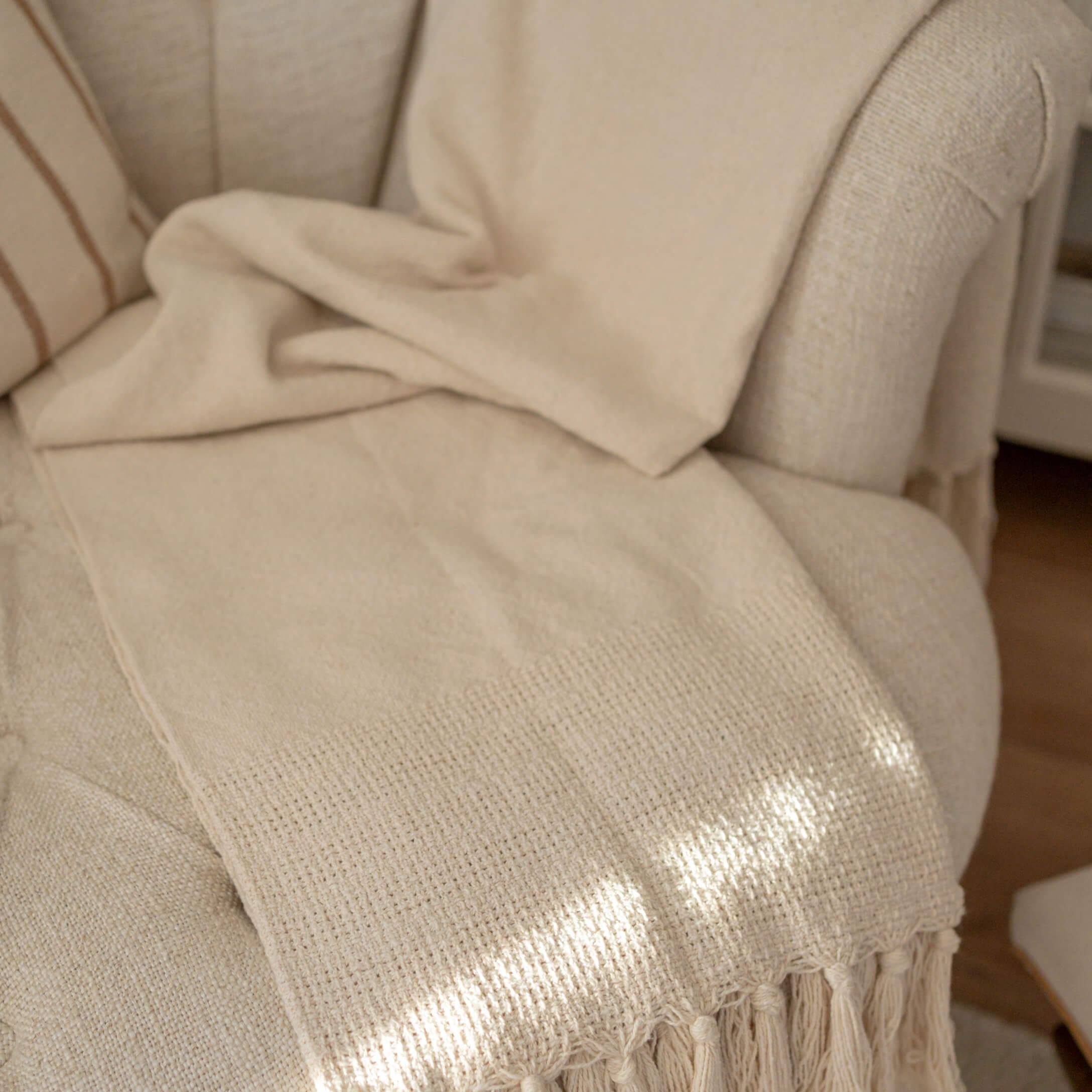 Beige Decke mit Fransen auf hellem Sessel, weiches Material für Wohnkultur und Entspannung