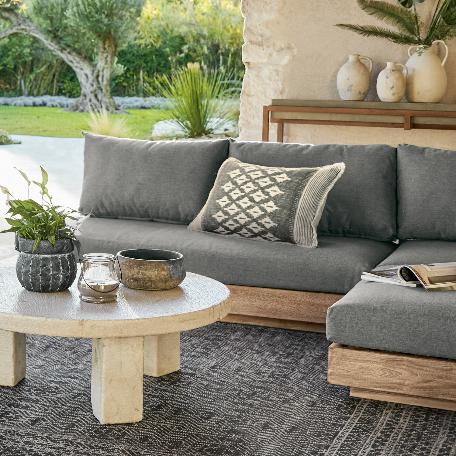 Graues Sofa mit Holzsockel und dekorativem Kissen auf der Terrasse mit Steintisch
