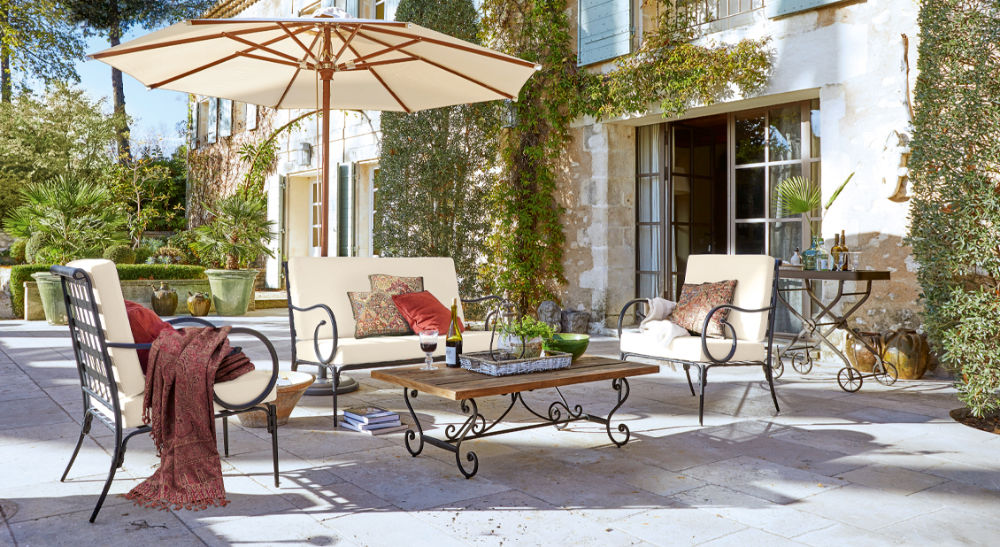Gartenmöbel-Set mit Metallrahmen und cremefarbenen Polstern auf steinerner Terrasse mit Sonnenschirm