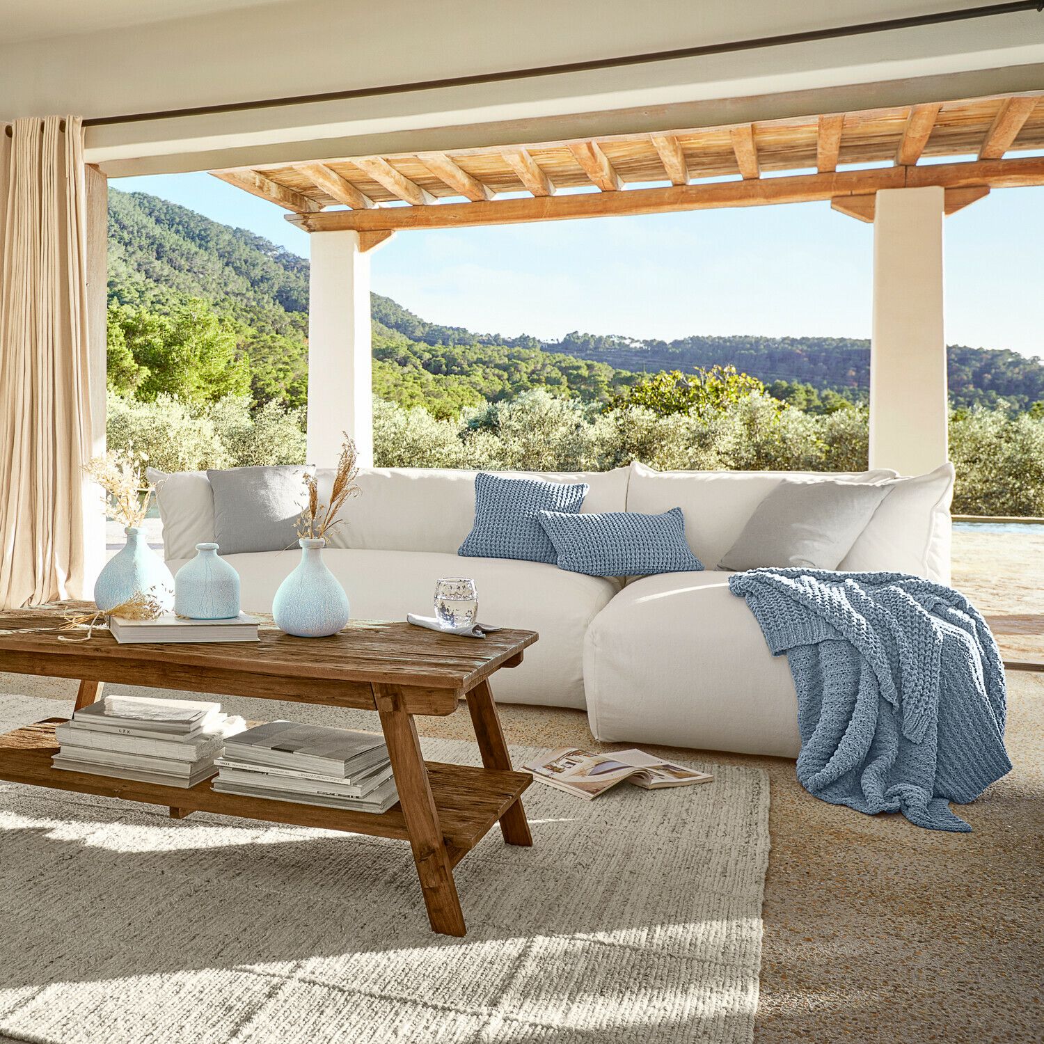 Gemütliches weisses Sofa mit blauem Strickplaid und Kissen auf Terrasse mit grünem Ausblick