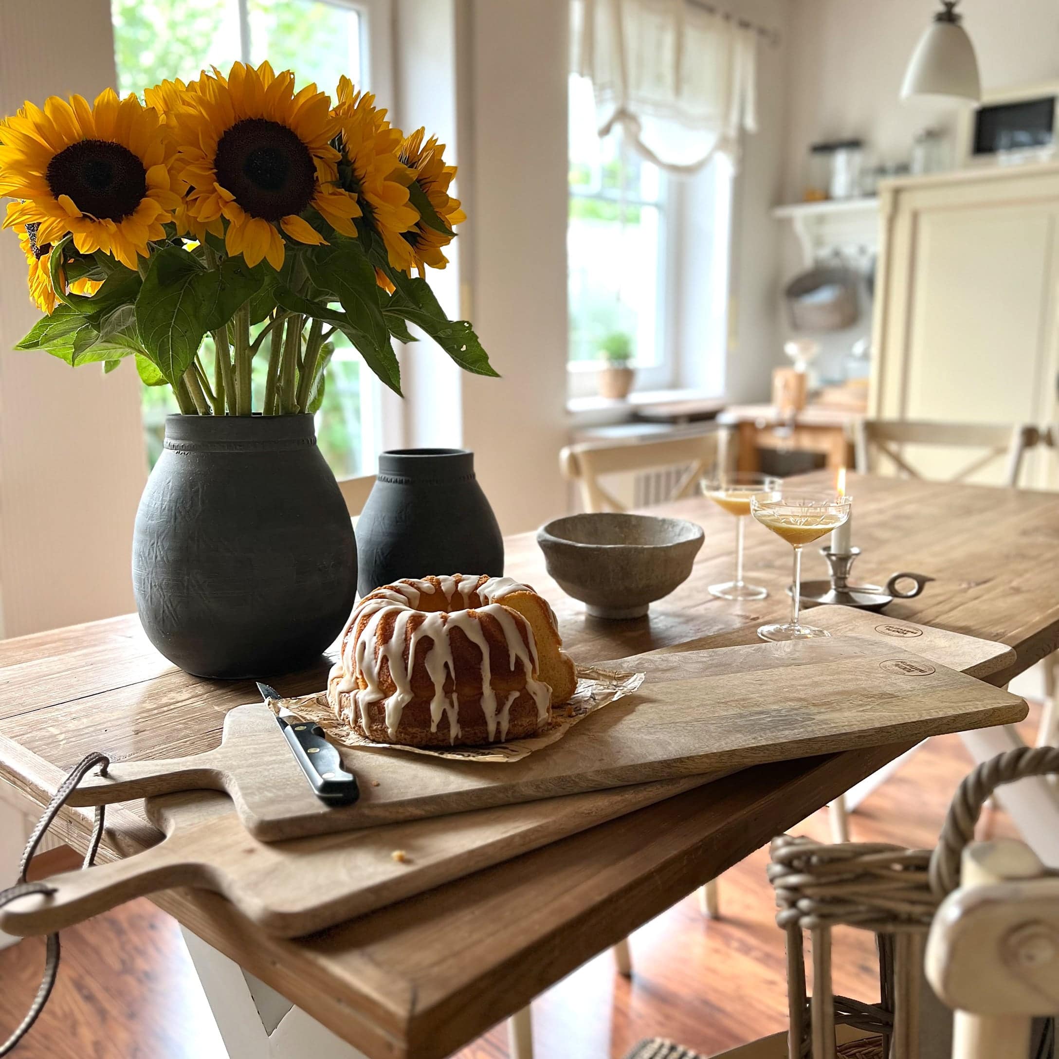 Holz-Schneidebrett mit Kuchen und schwarze Vase mit gelben Sonnenblumen auf Holztisch in der Küche