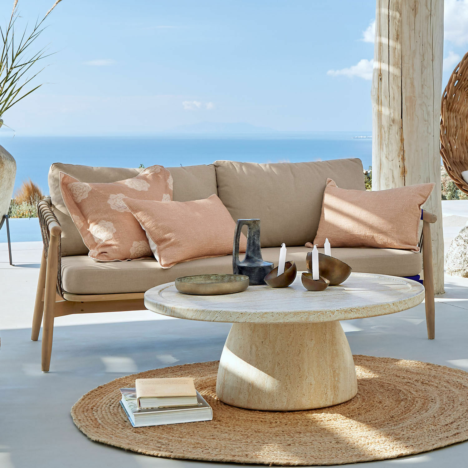 Sofa FSC®-100% Thornwick Beiges Sofa mit Kissen und runder Steintisch auf Terrasse mit Meerblick
