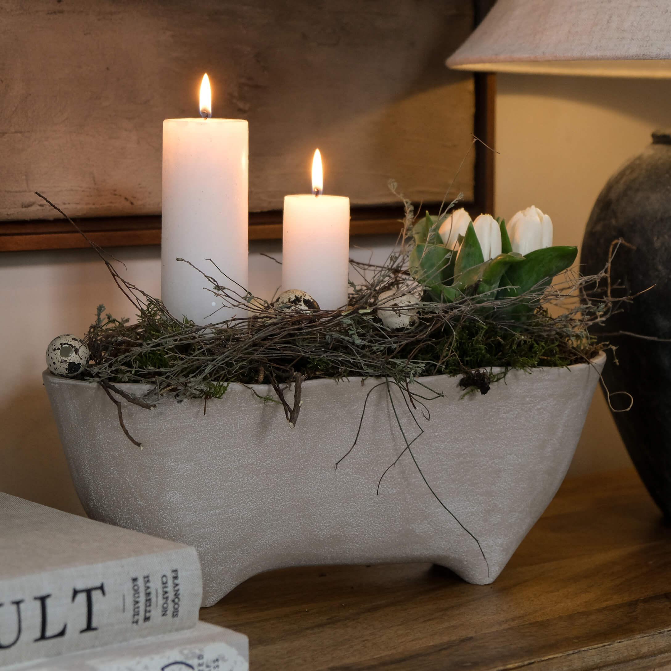 Graue Keramikschale mit weissen Kerzen, Zweigen und weissen Tulpen auf Holztisch als Dekoration