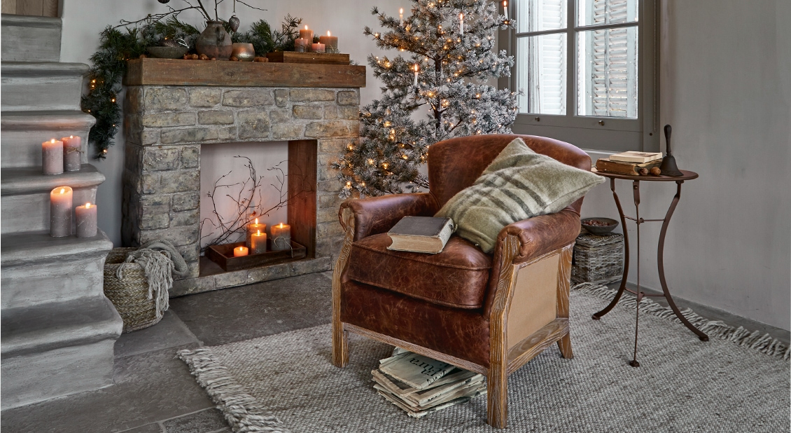 Gemütliches Wohnzimmer mit braunem Ledersessel, Steinkamin und weihnachtlicher Dekoration mit Baum und Kerzen.
