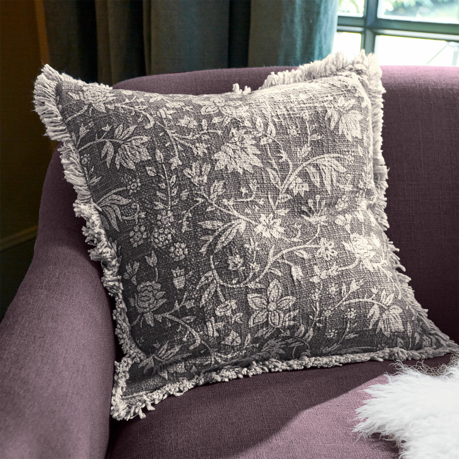 Kissenhülle Jorelise Graues Dekokissen mit weissem Blumenmuster und Fransen auf violettem Sofa