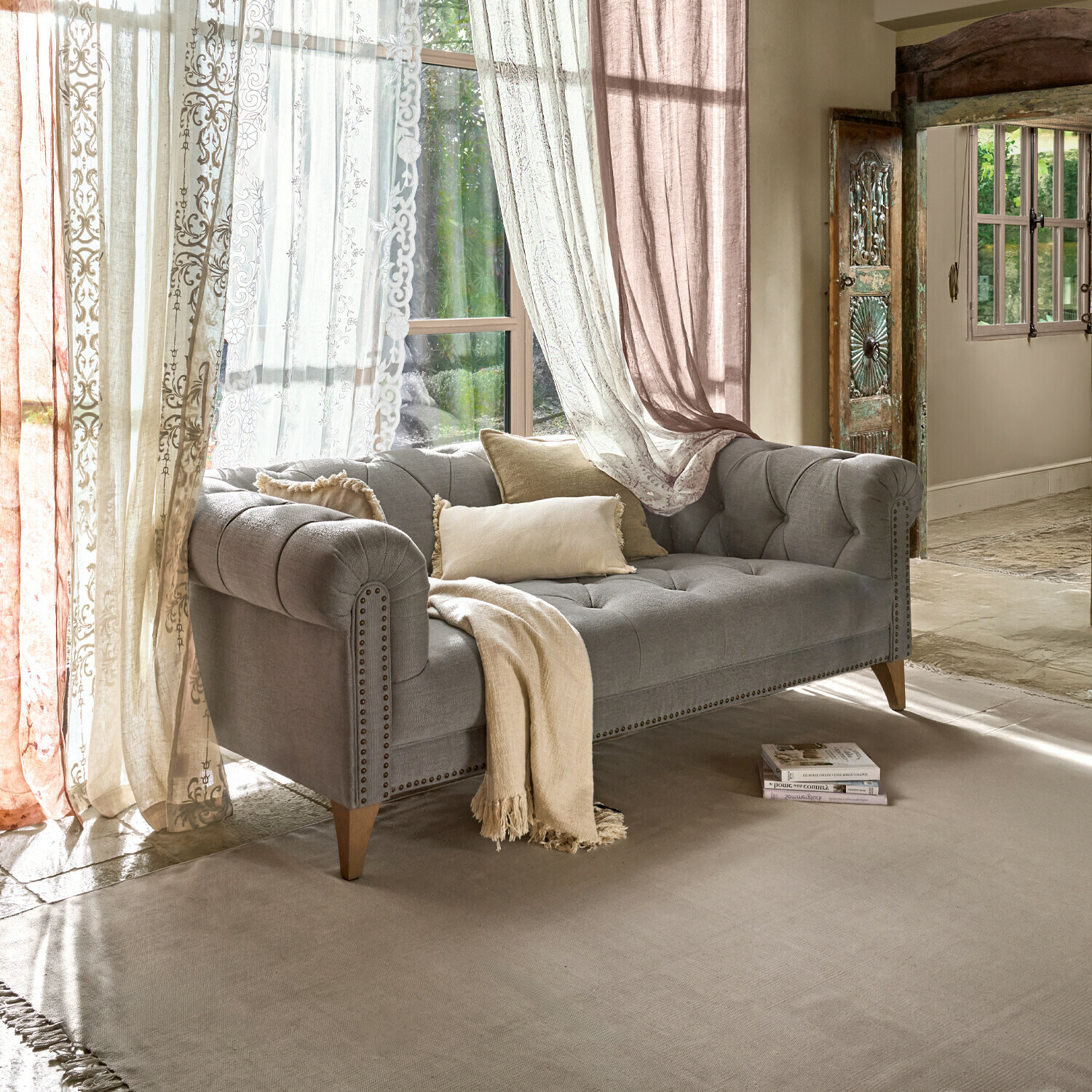 Grau gepolstertes Sofa mit Holzbeinen und beigen Kissen in hellem Wohnzimmer mit Vorhängen