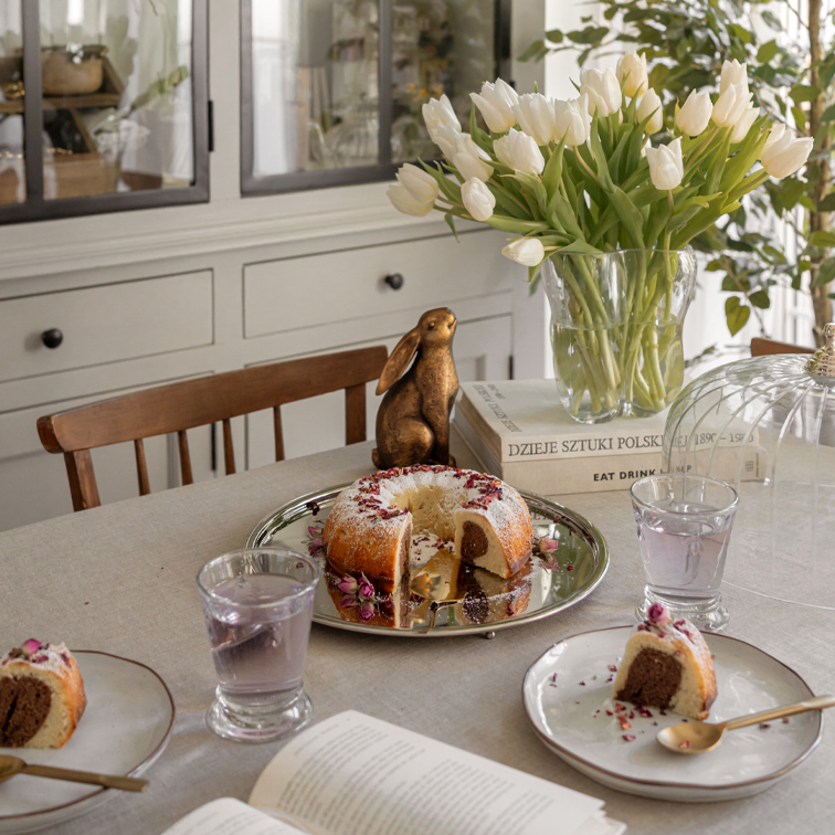 Tisch mit Marmorkuchen auf silbernem Tablett, weisse Tulpen in Glasvase und dekorativem Hasen